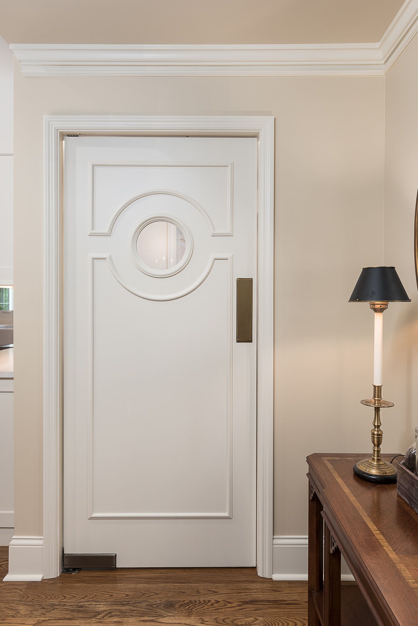 A white door with a round window is in a room next to a lamp.