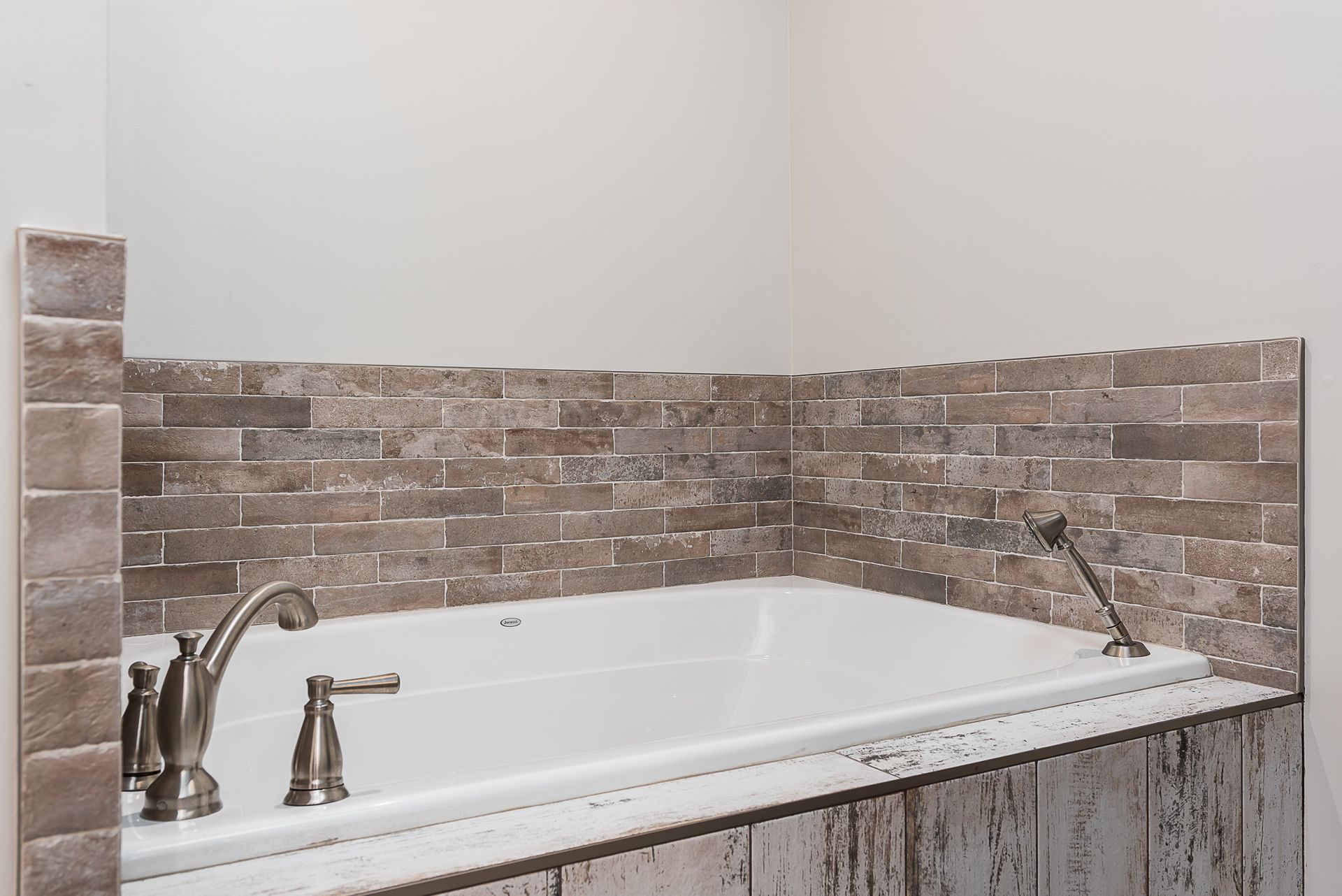 A bathtub in a bathroom with a brick wall behind it.