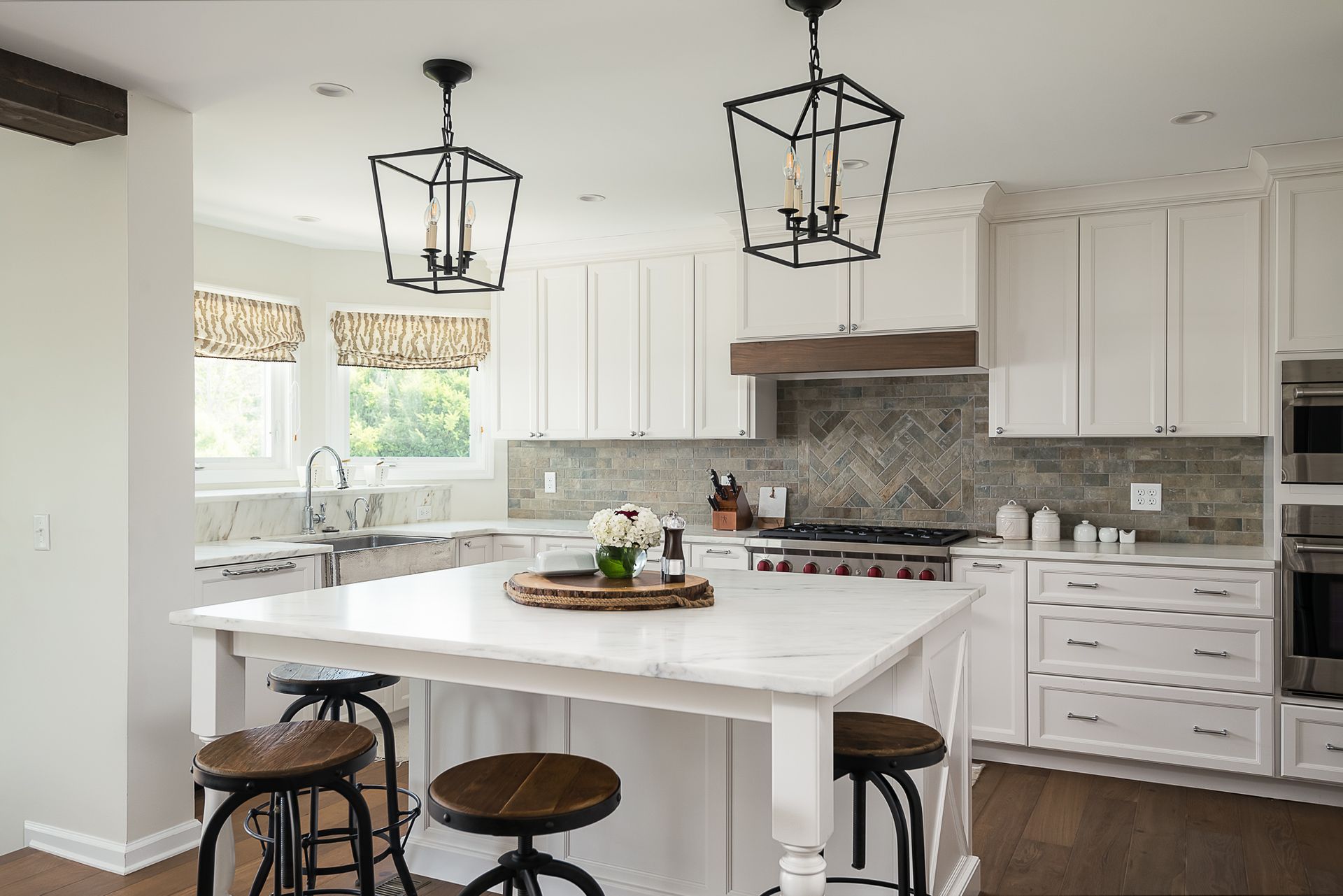 A kitchen with white cabinets , a large island , stools and a stove.