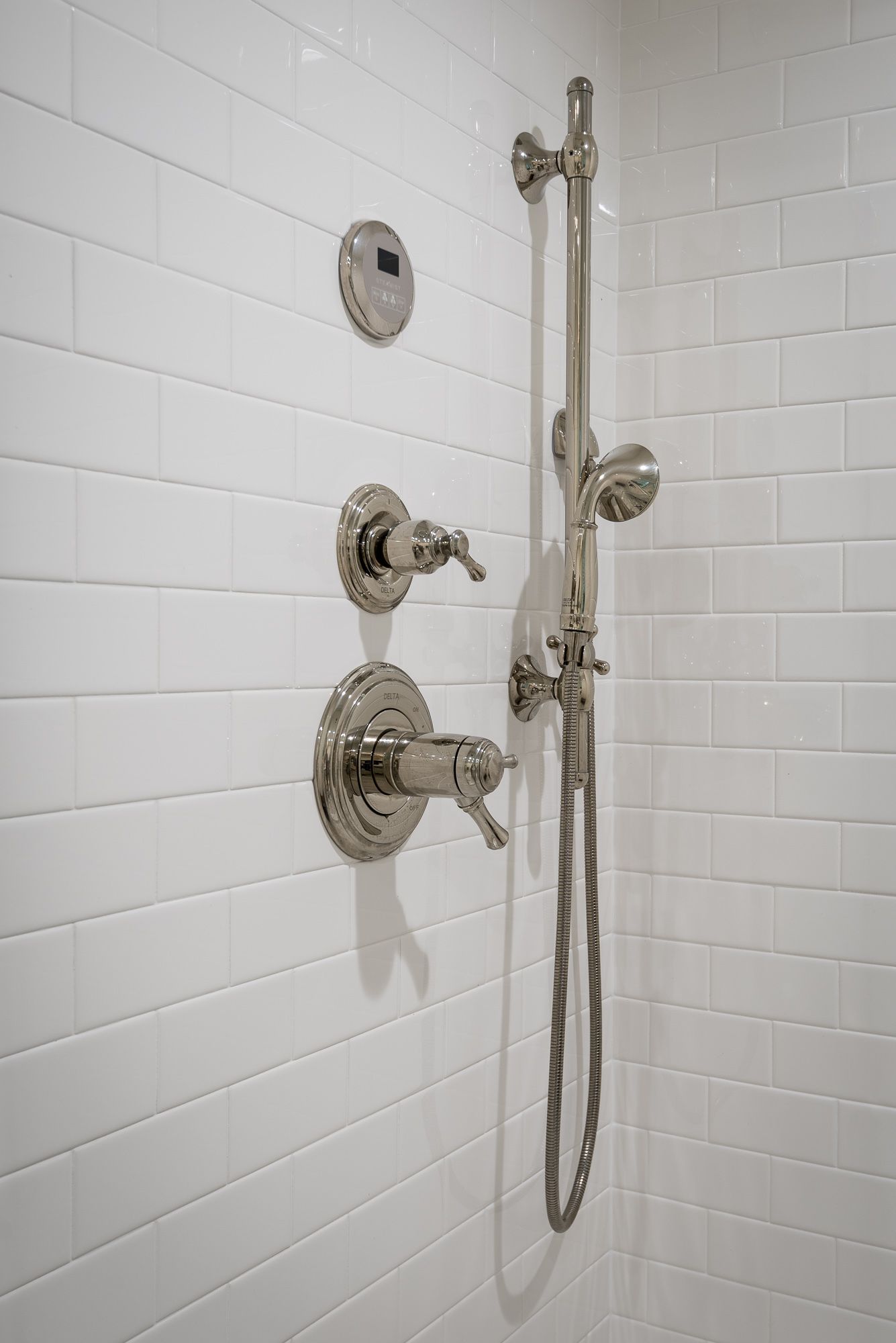 A close up of a shower head on a white tiled wall.