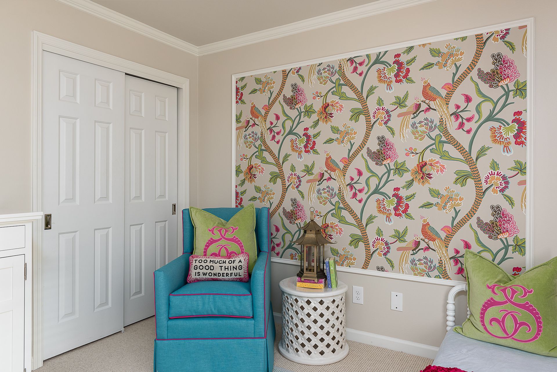 A room with a chair , table , and floral wallpaper on the wall.