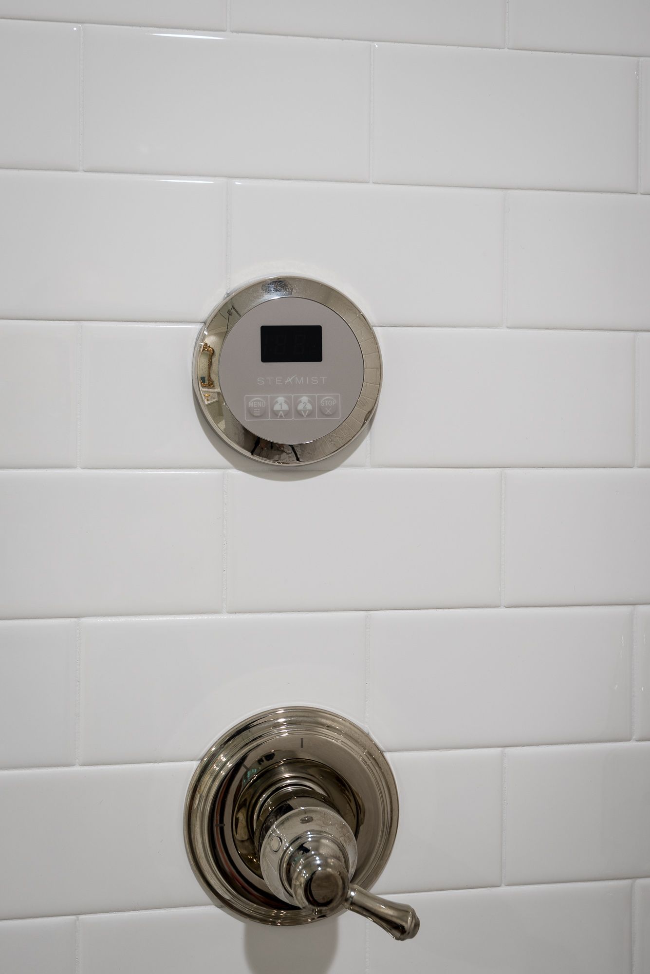 A close up of a shower faucet on a white tiled wall.