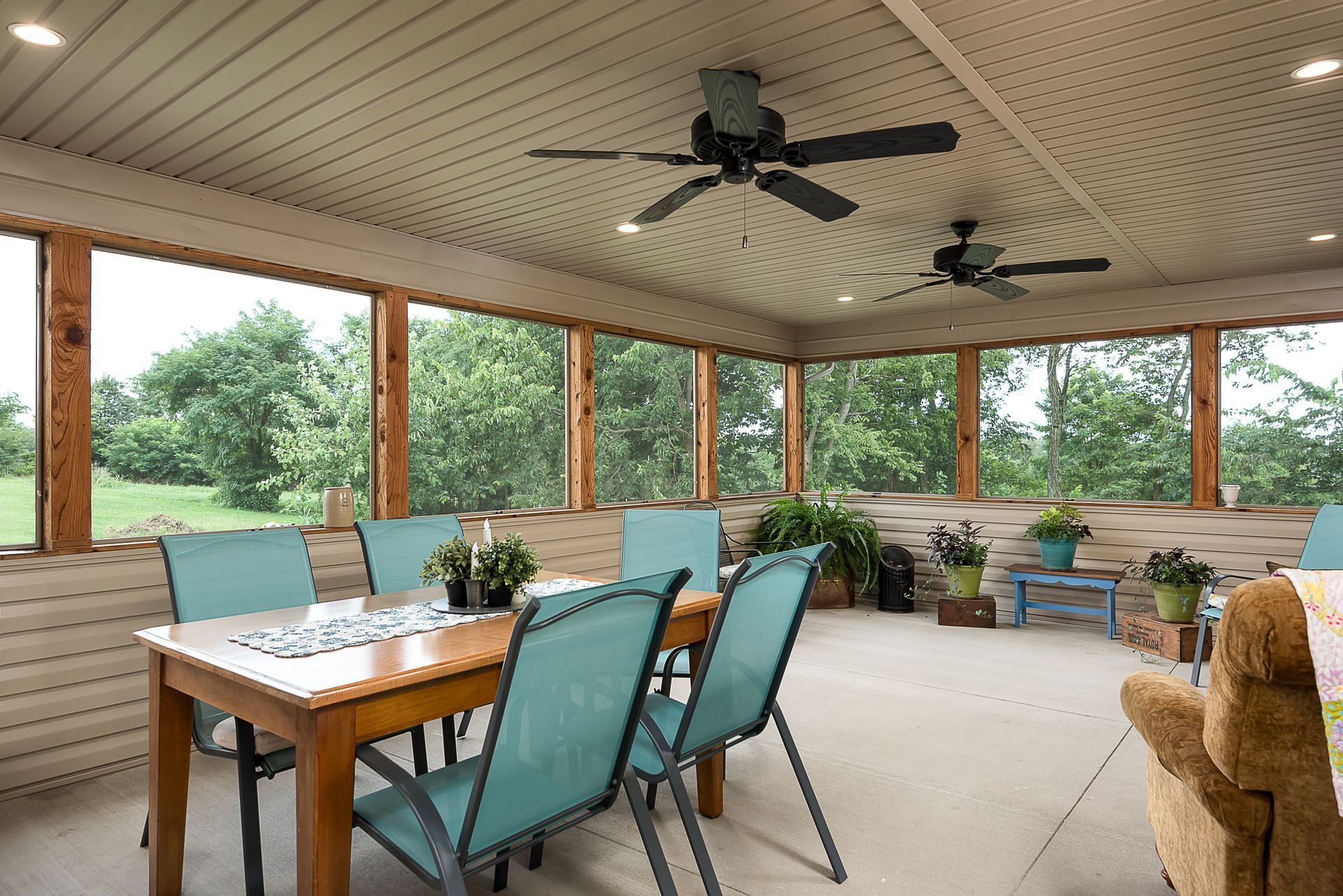 A screened in porch with a table and chairs and a ceiling fan.