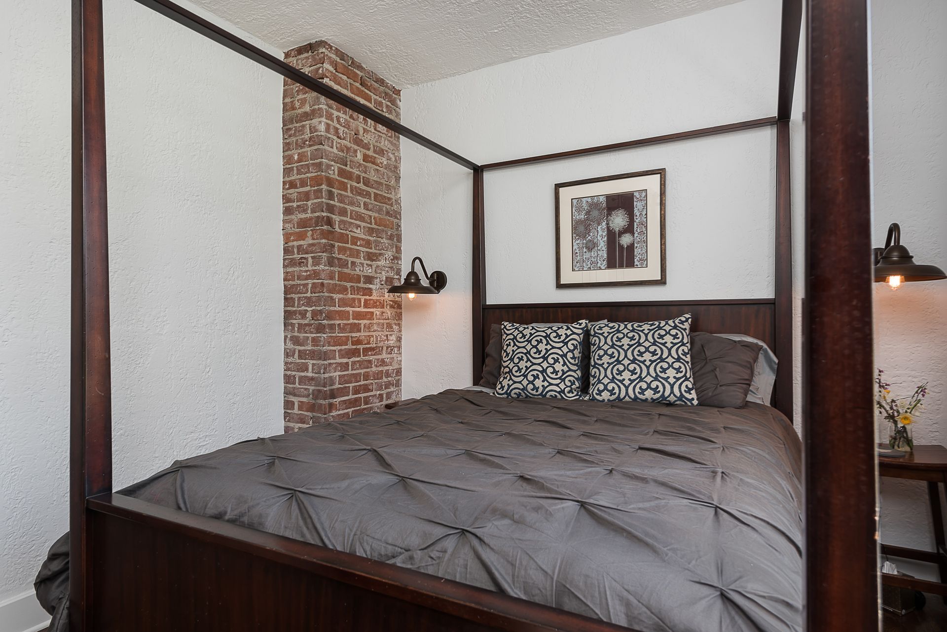 A bedroom with a four poster bed and a brick wall