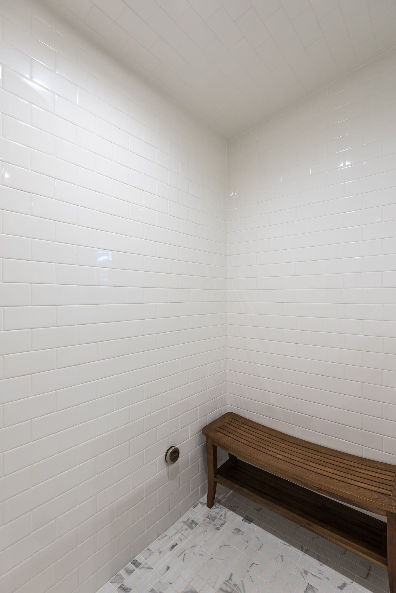 A bathroom with white tiles and a wooden bench.