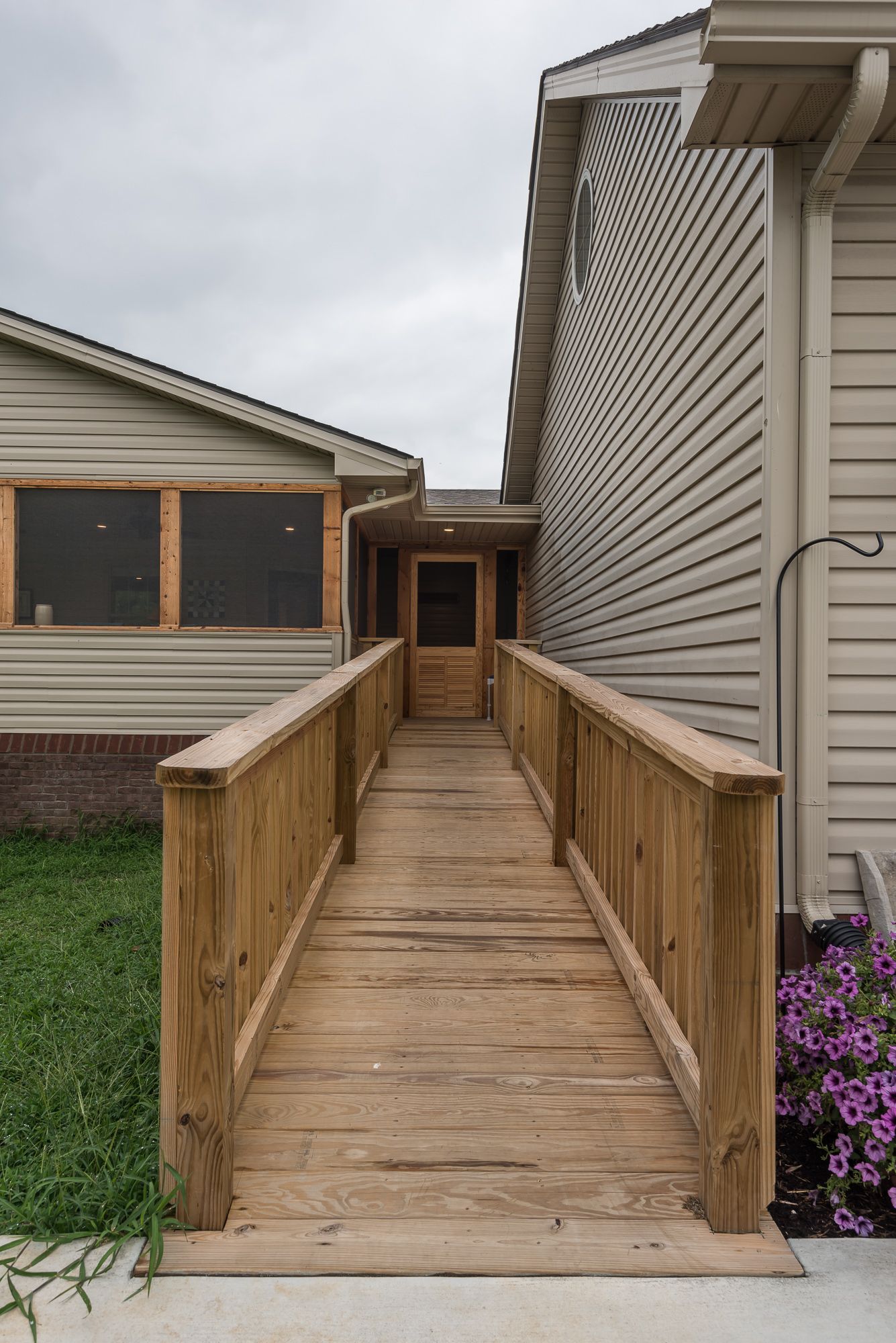 A wooden ramp leading to a house with a screened in porch.