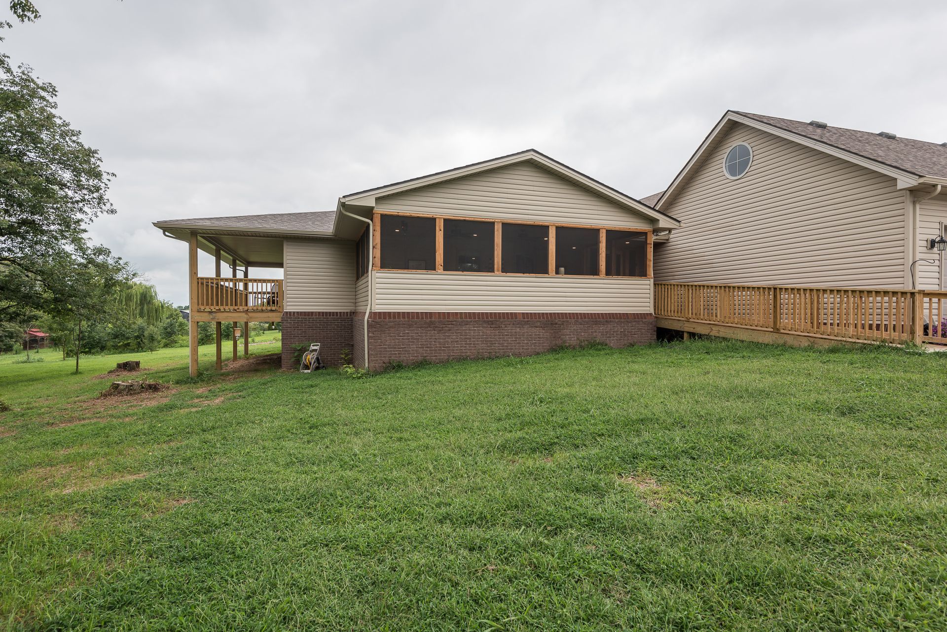A house with a screened in porch and a large lawn in front of it.