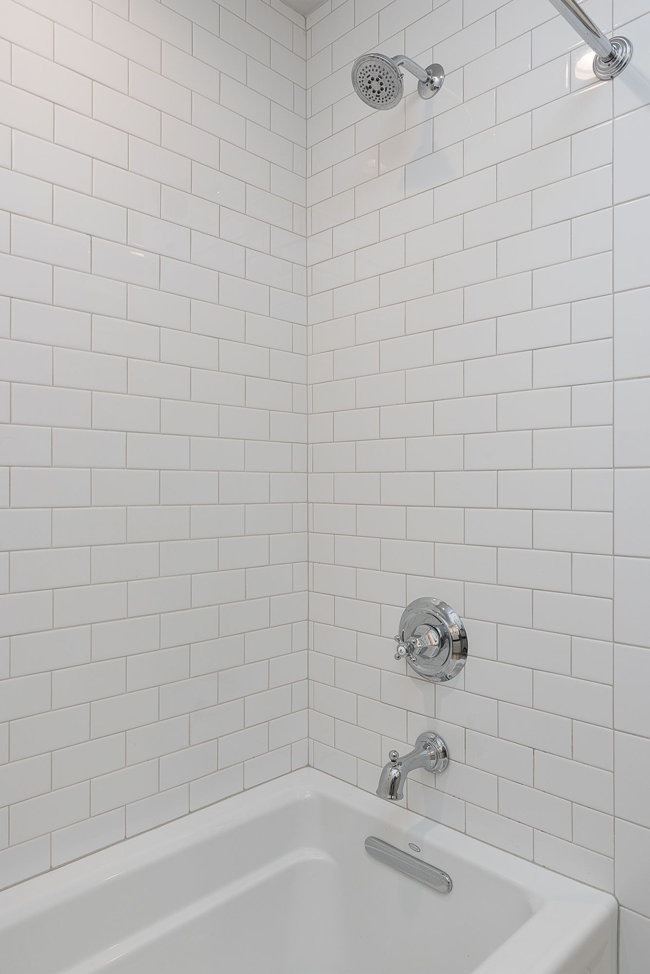 A bathroom with white tiles and a bathtub and shower.