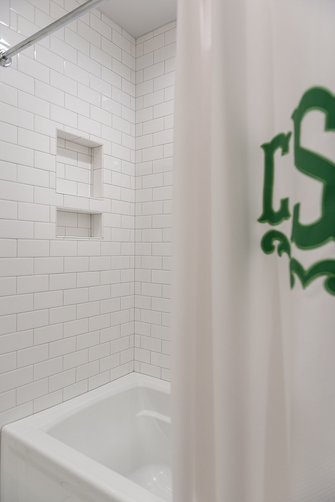 A bathroom with white tiles and a green shower curtain.