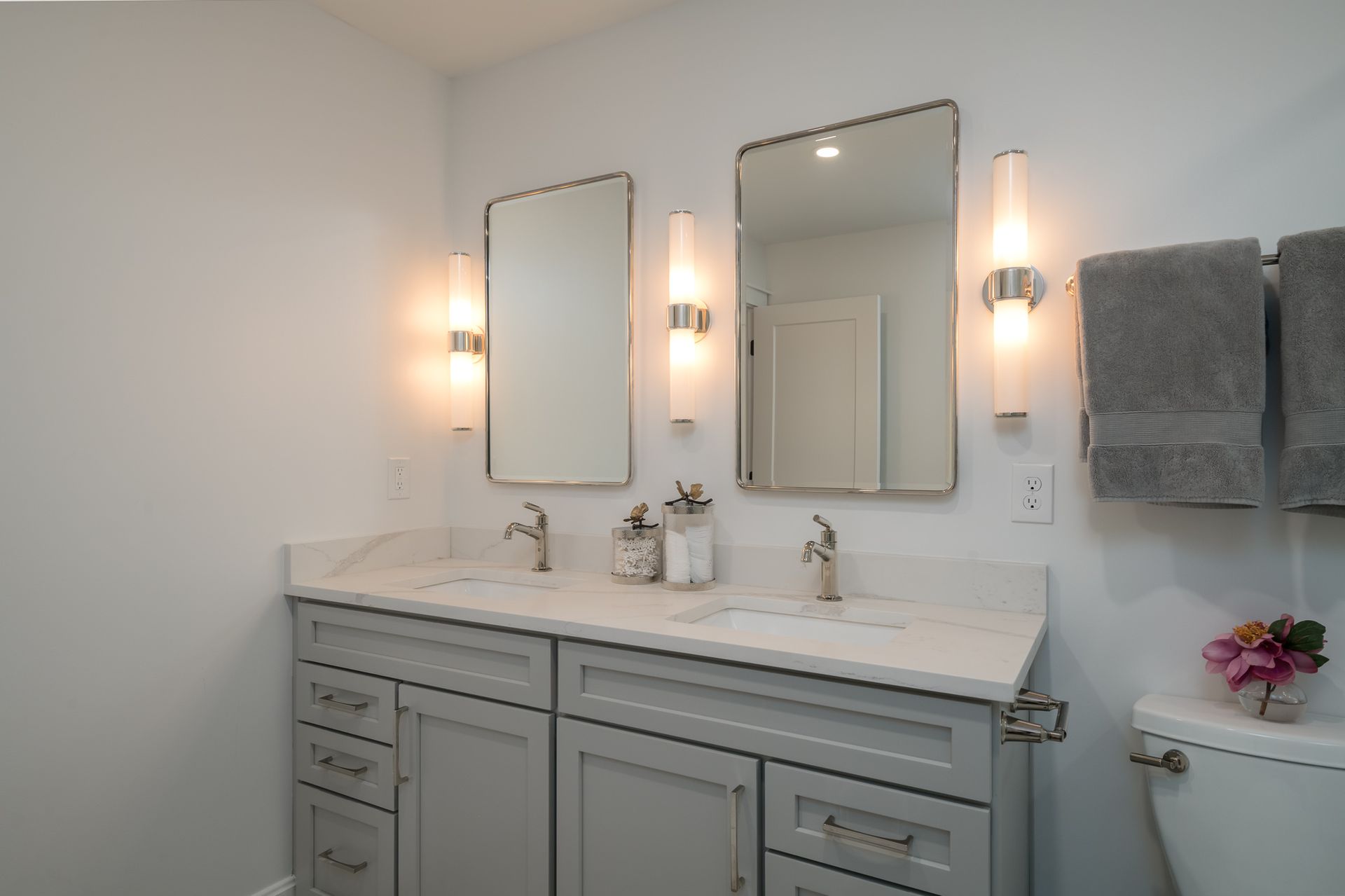 A bathroom with two sinks , two mirrors and a toilet.