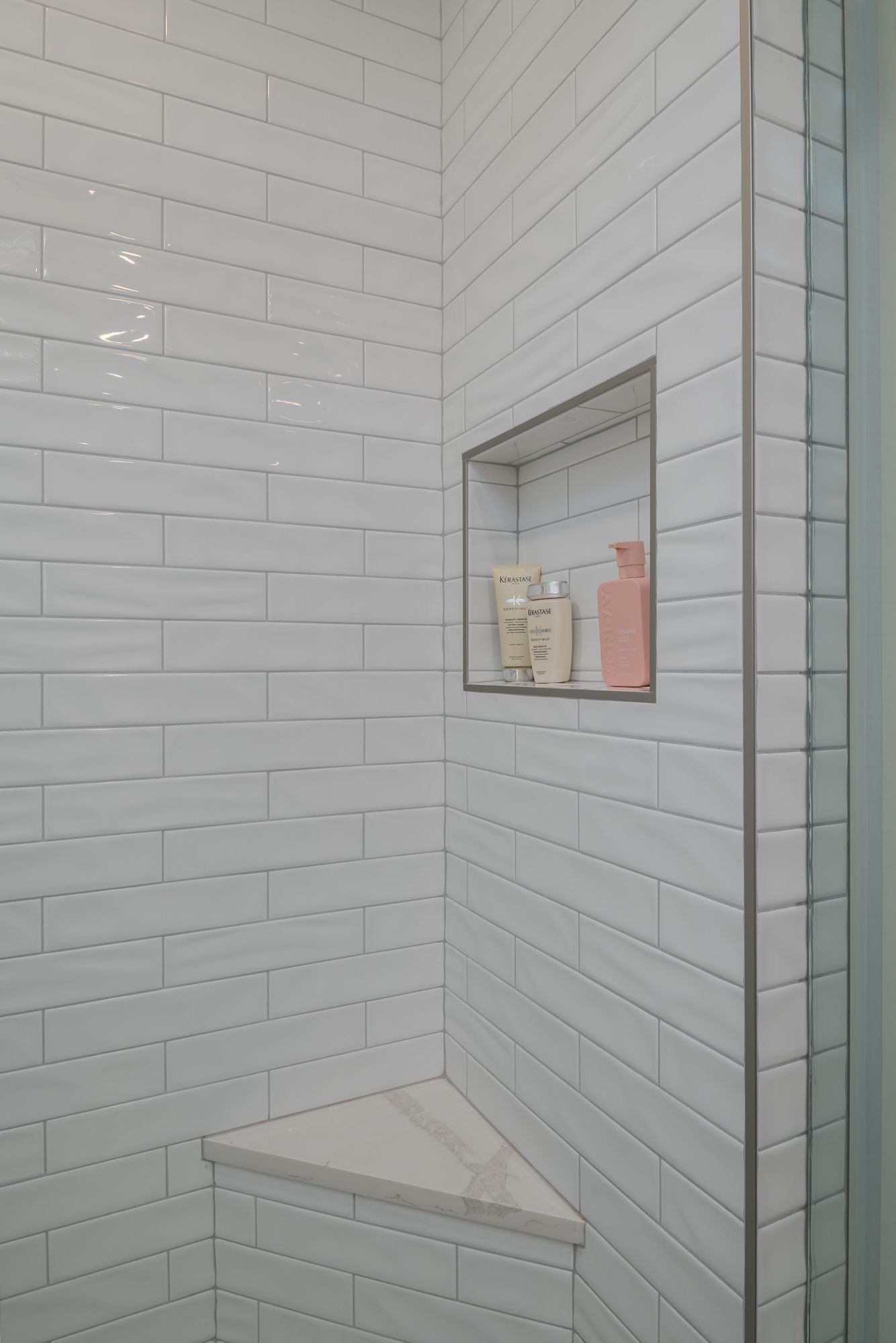 A shower with white tiles and a corner shelf.