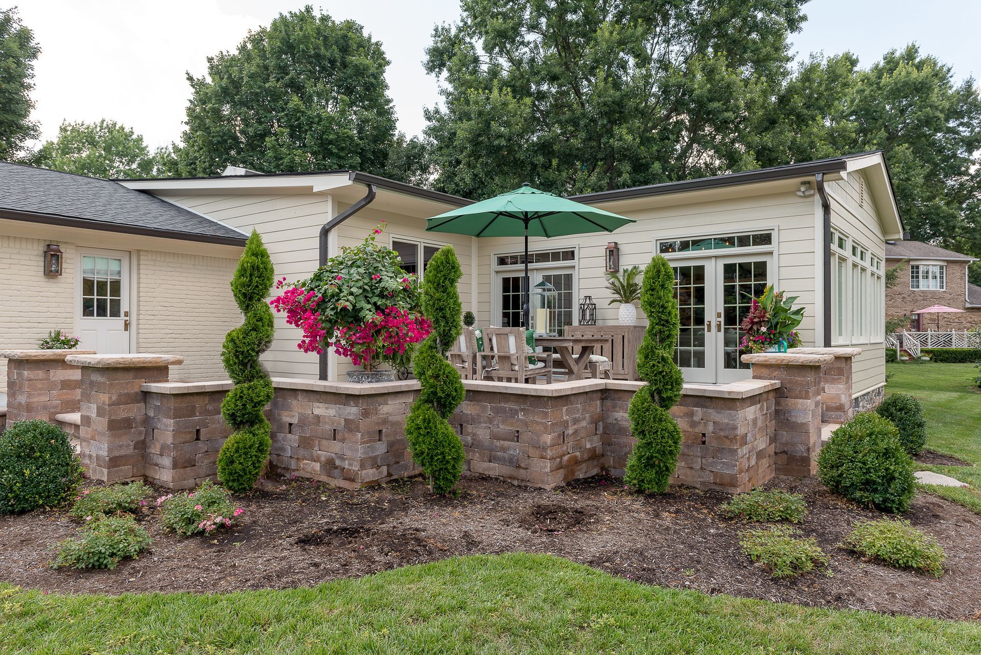 A house with a patio and a green umbrella in front of it.