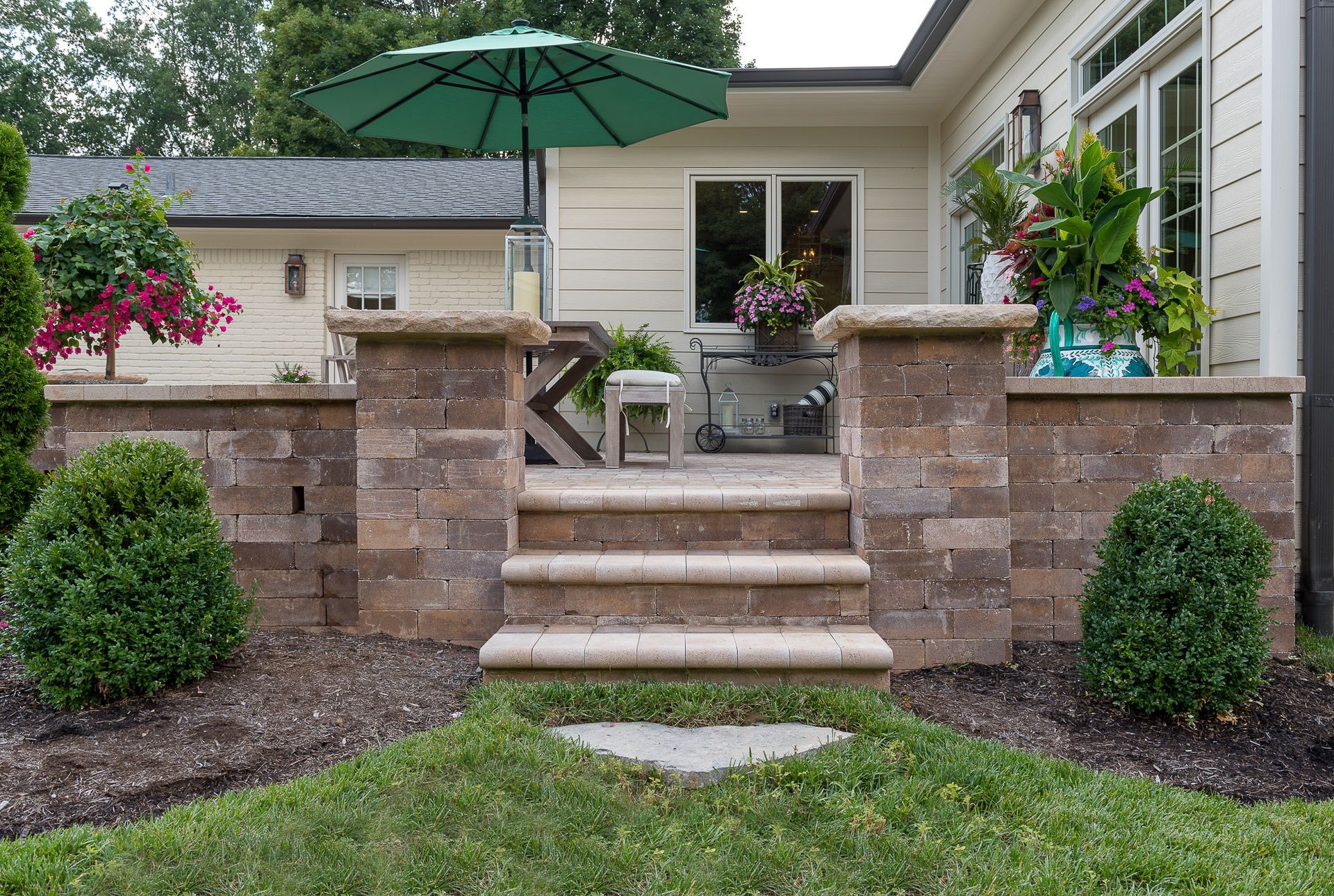 A patio with stairs and a green umbrella in front of a house.