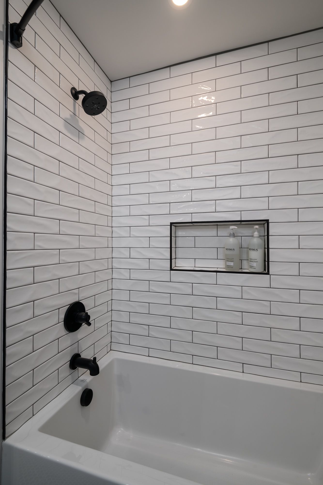A bathroom with white brick tiles and a bathtub.
