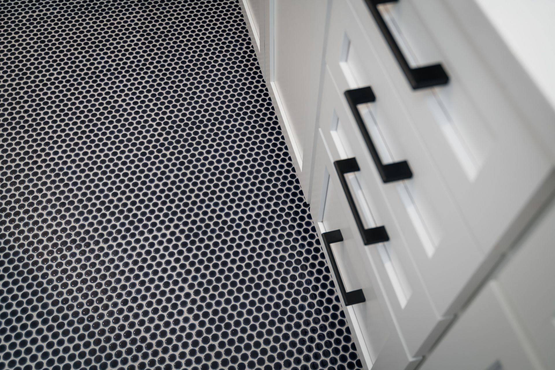 A black and white tile floor with white cabinets and black handles.
