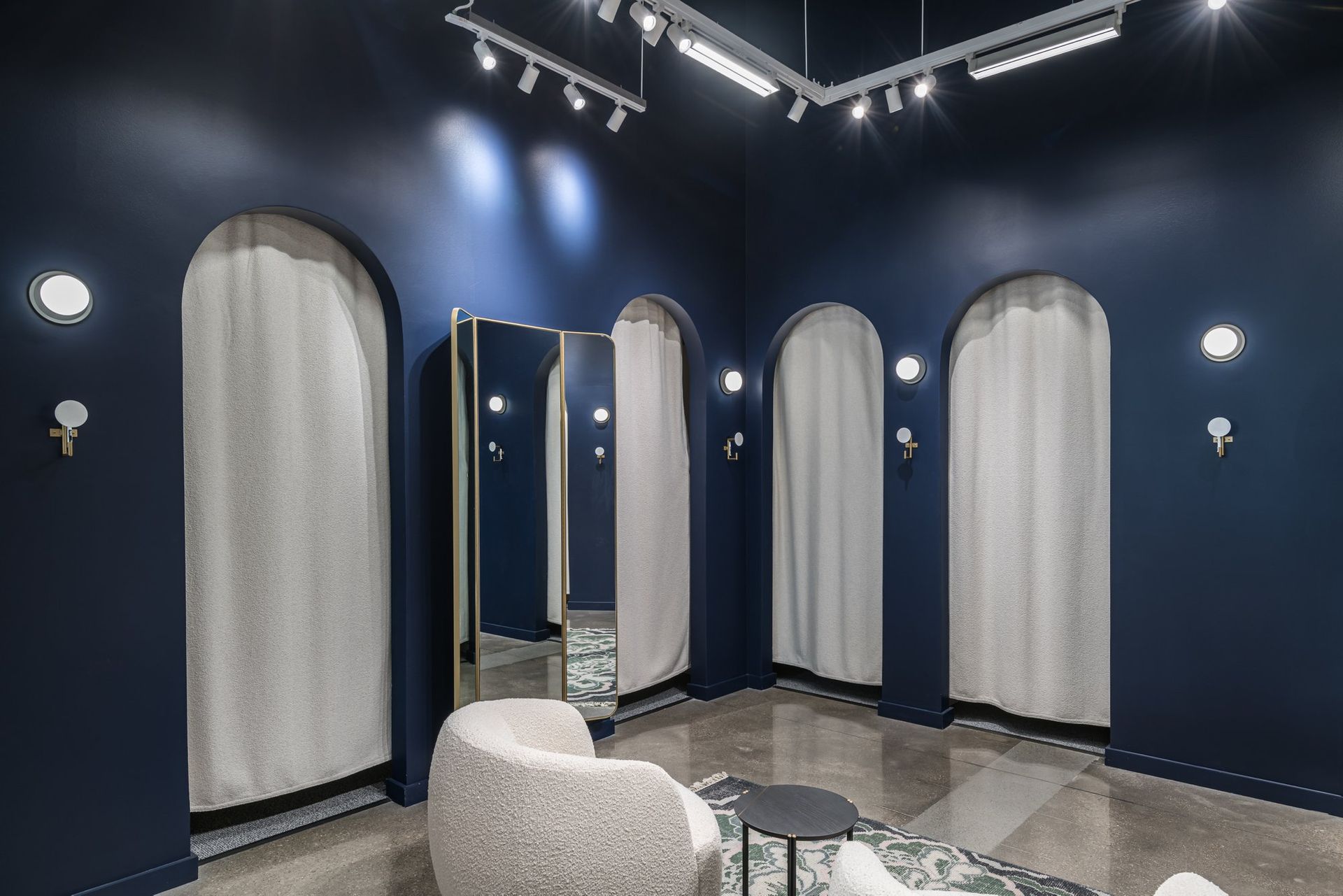 A dressing room with blue walls , white curtains , a chair and a mirror.