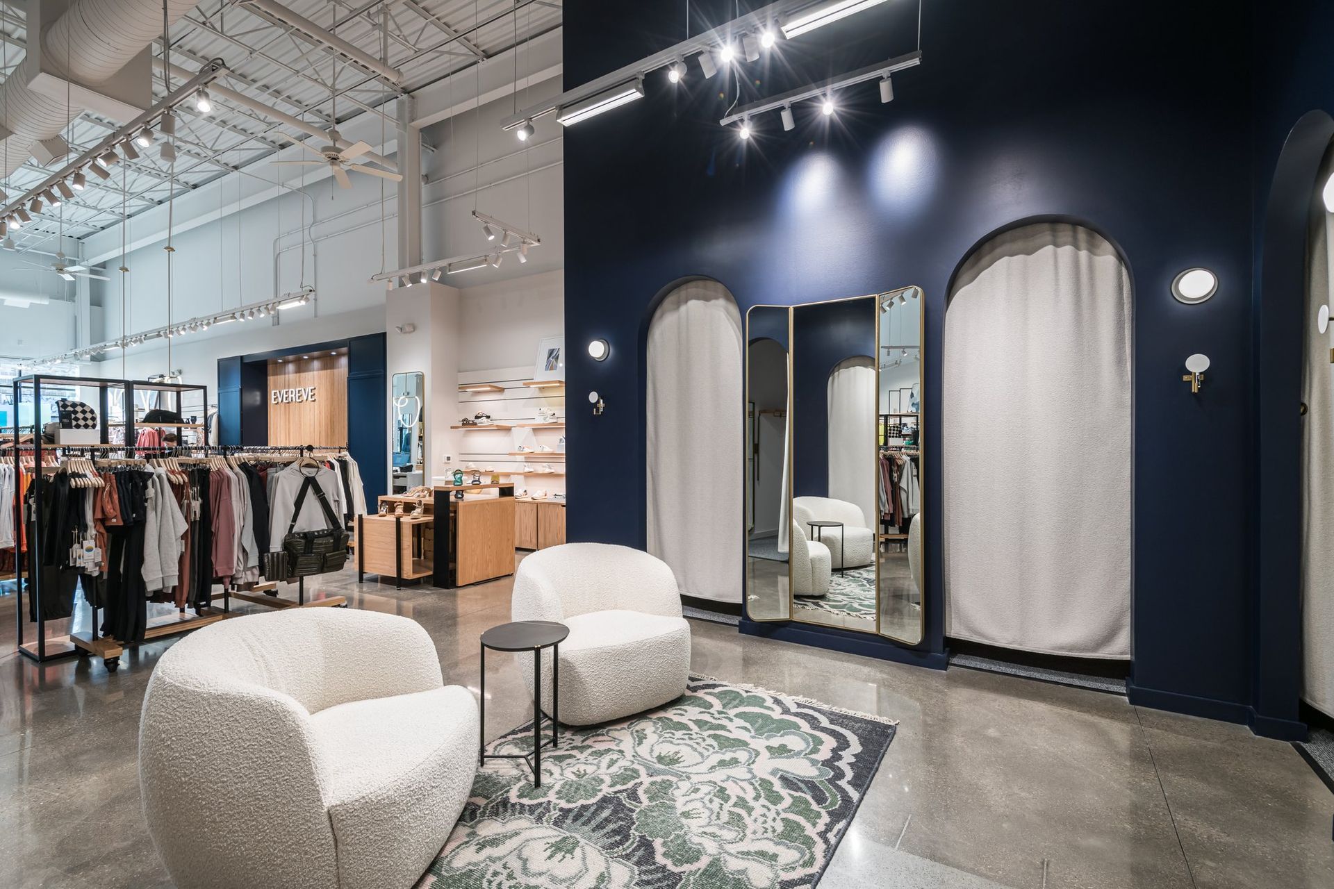 There are two chairs and a couch in the dressing room of a clothing store.
