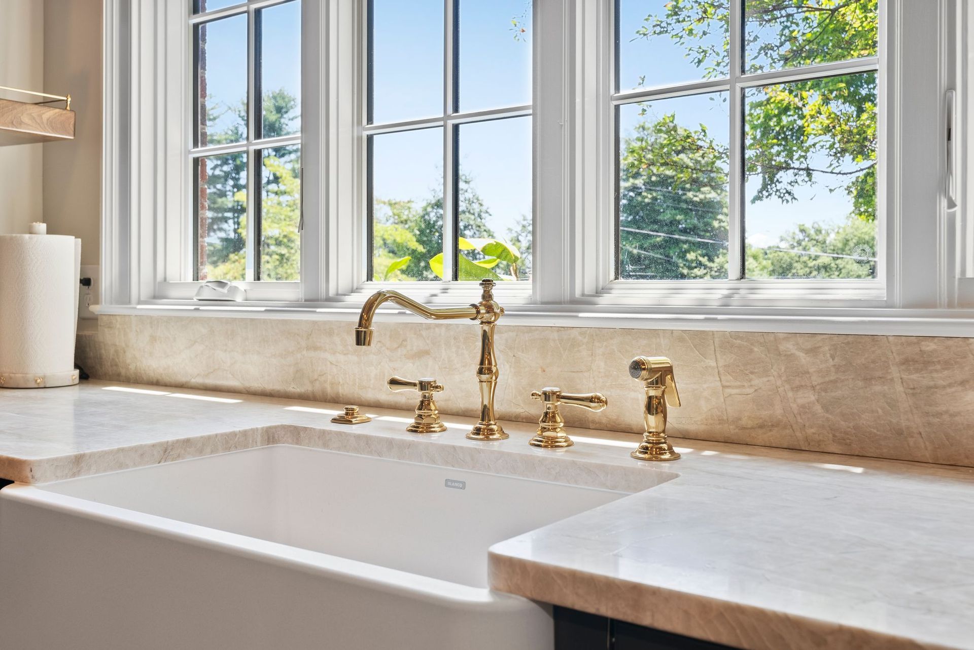 A kitchen sink with a gold faucet and a window.