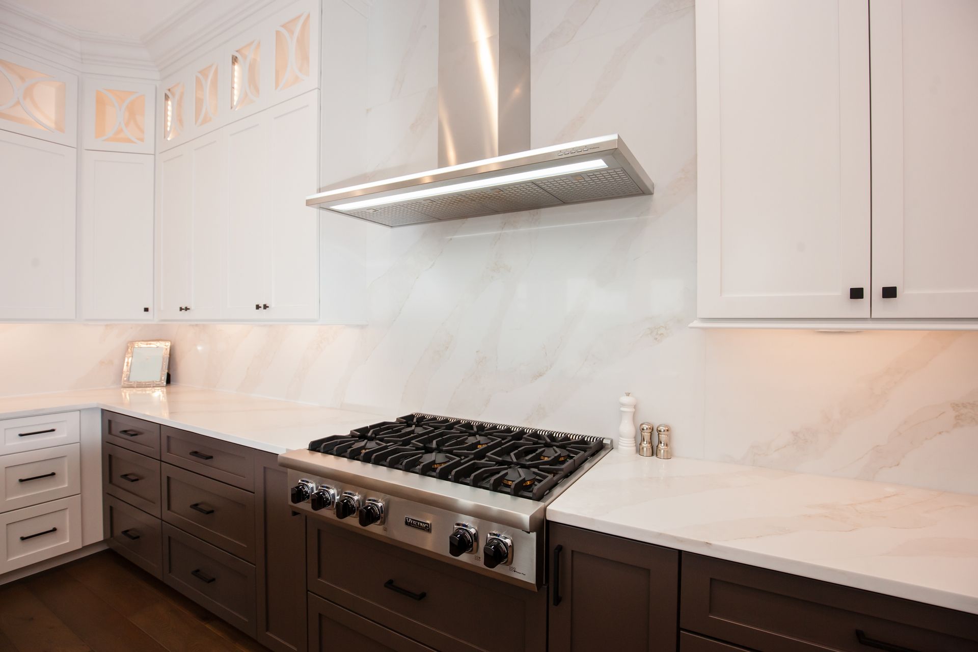 A kitchen with a stove top oven , stainless steel hood , and white cabinets.