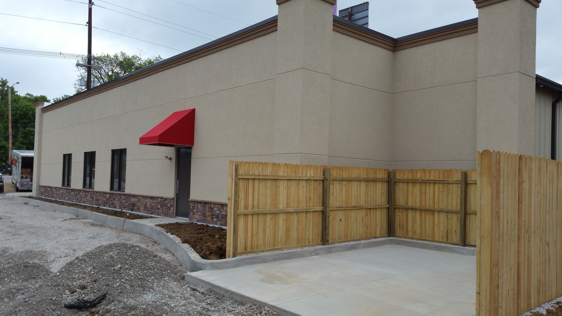 A building under construction with a red awning and a wooden fence.