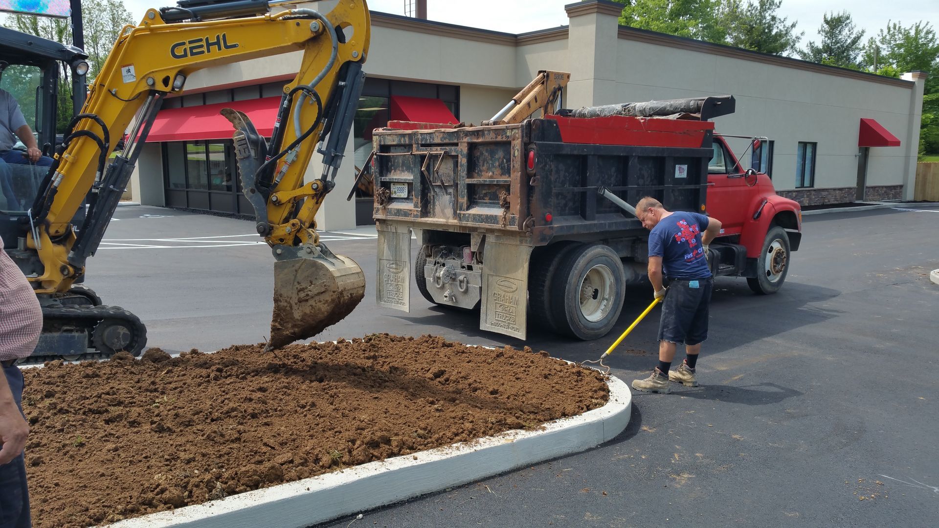 A man is raking dirt in front of a dump truck.