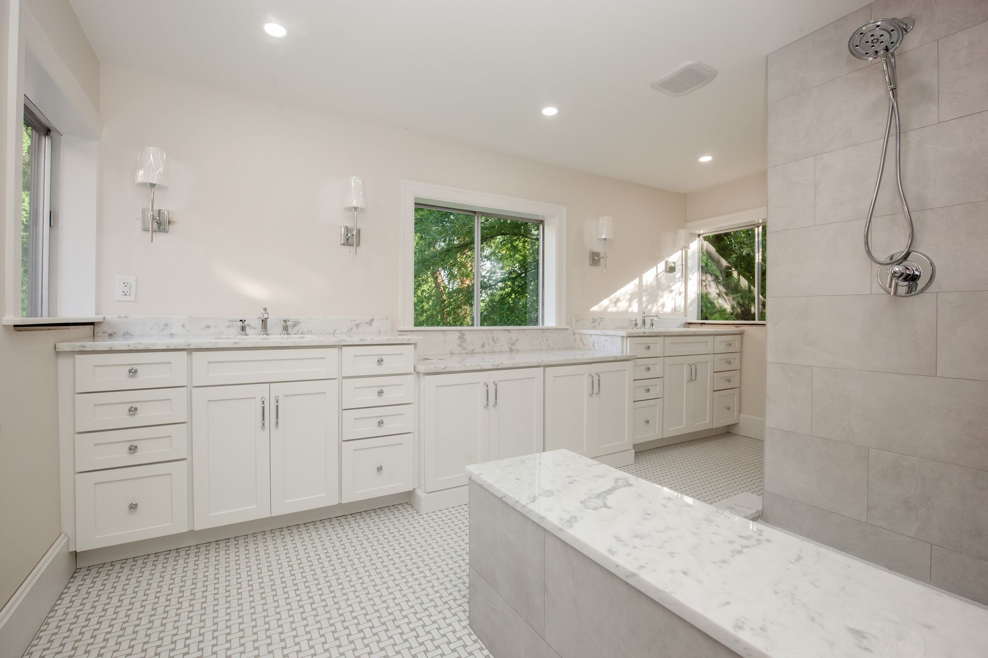 A bathroom with white cabinets , marble counter tops , and a walk in shower.