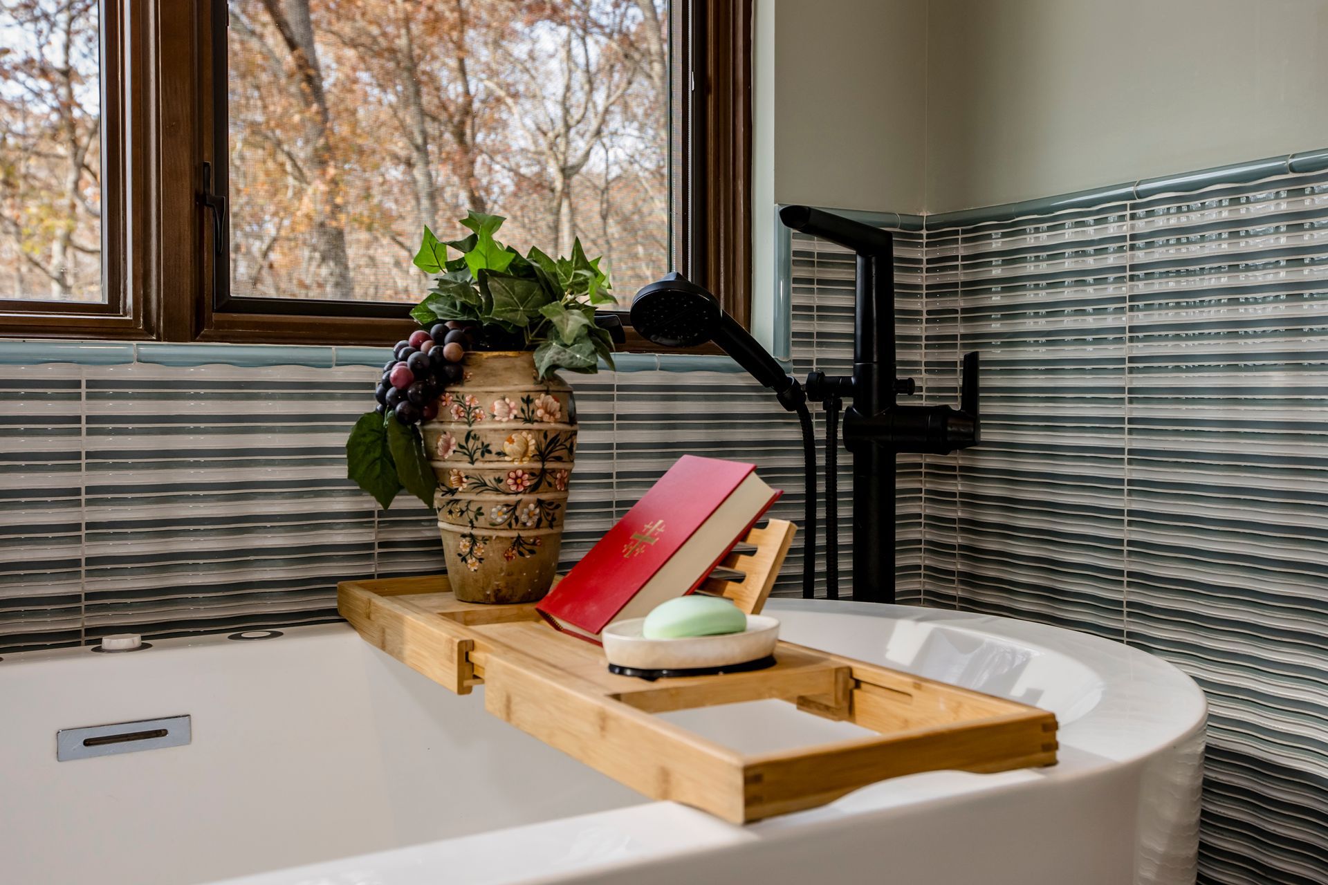 A bathtub with a wooden tray on it and a book on it.