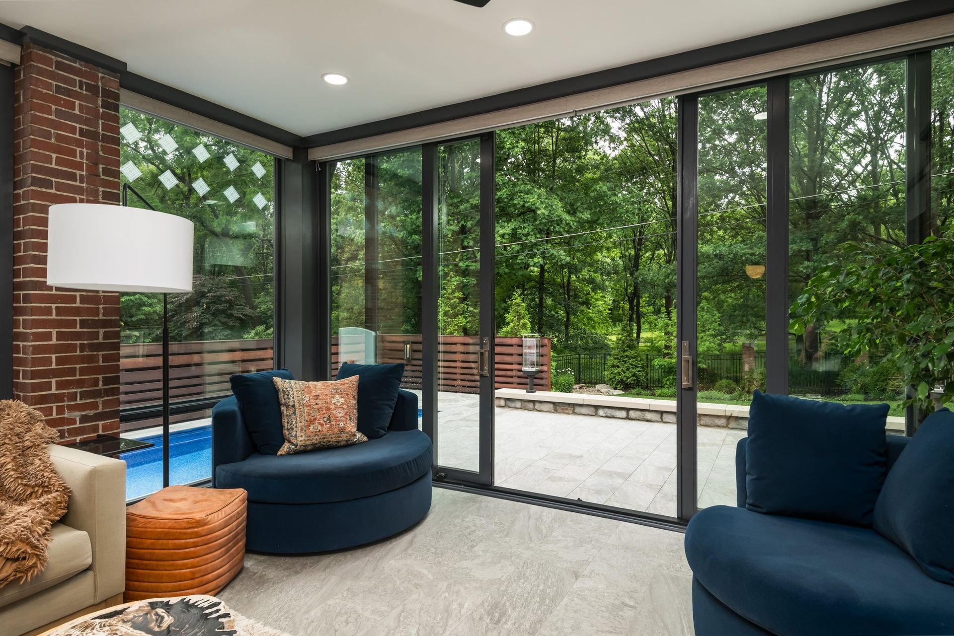 A living room with a couch , chair , lamp and sliding glass doors leading to a pool.