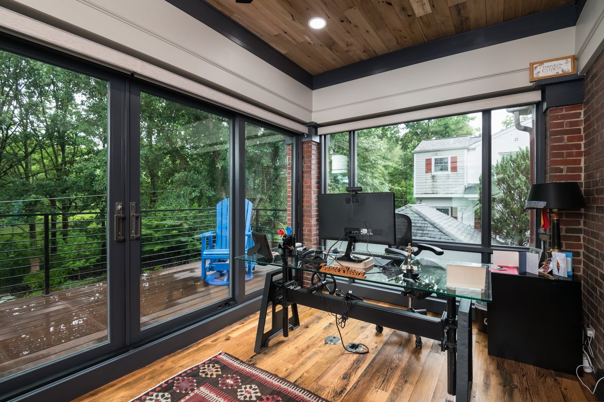 A home office with a desk , chair , computer and lots of windows.