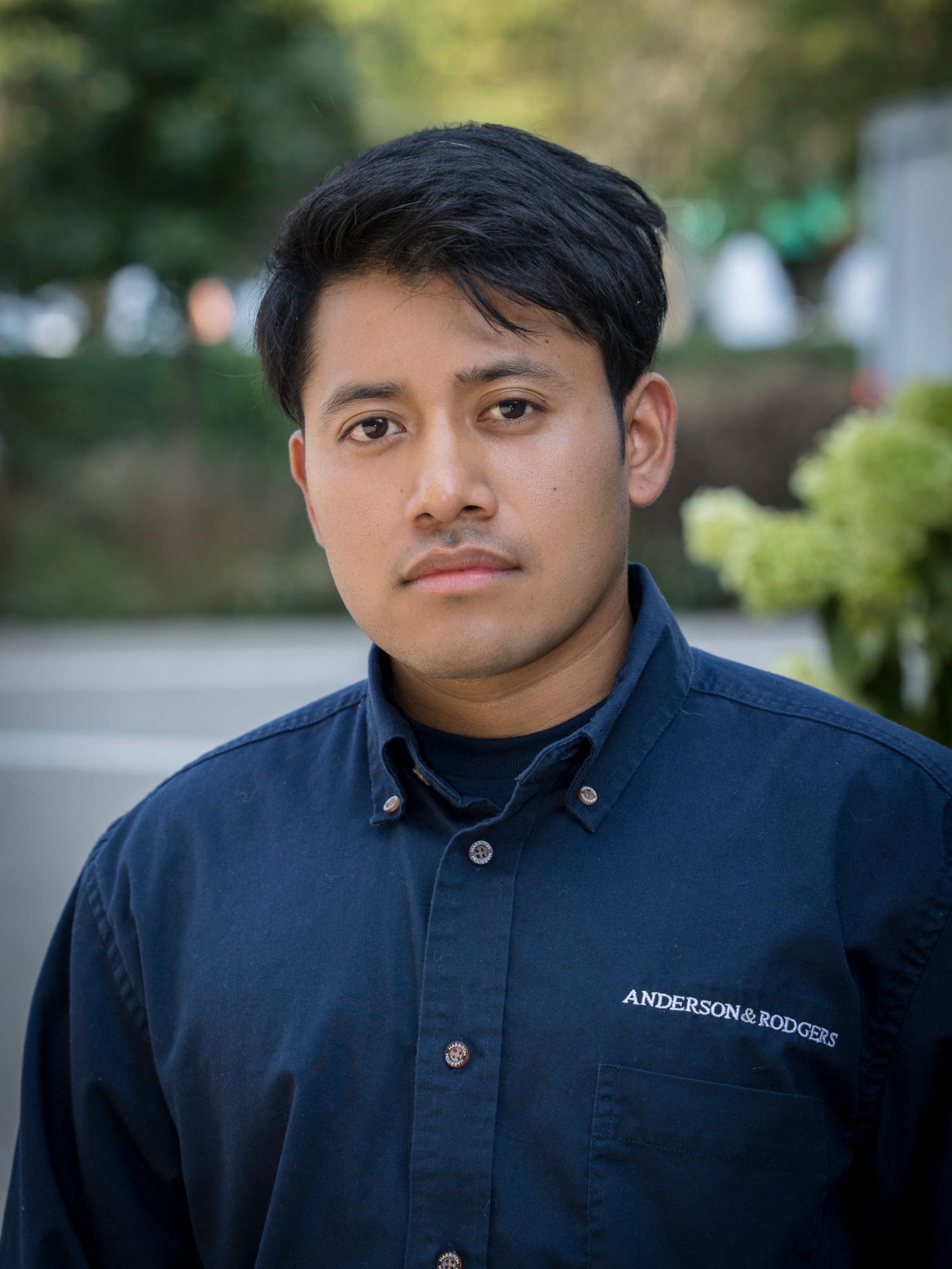 A young man wearing a blue jacket is standing in front of a building.