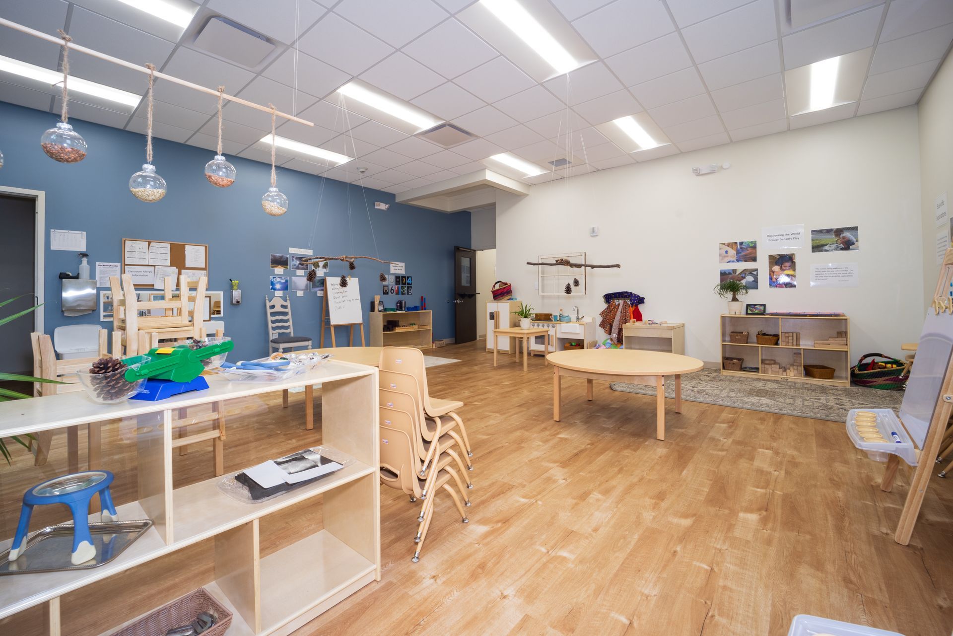 A large classroom with wooden floors and tables and chairs.