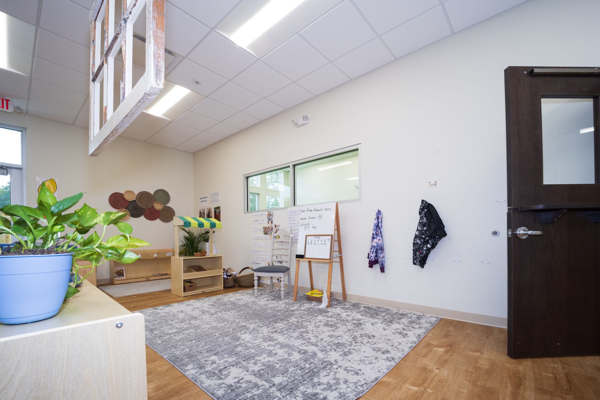 A room with a rug , a whiteboard , a potted plant and a door.
