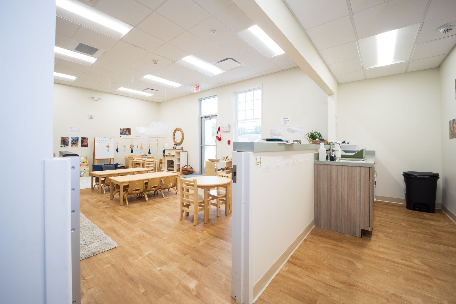 A classroom with wooden tables and chairs and a counter.
