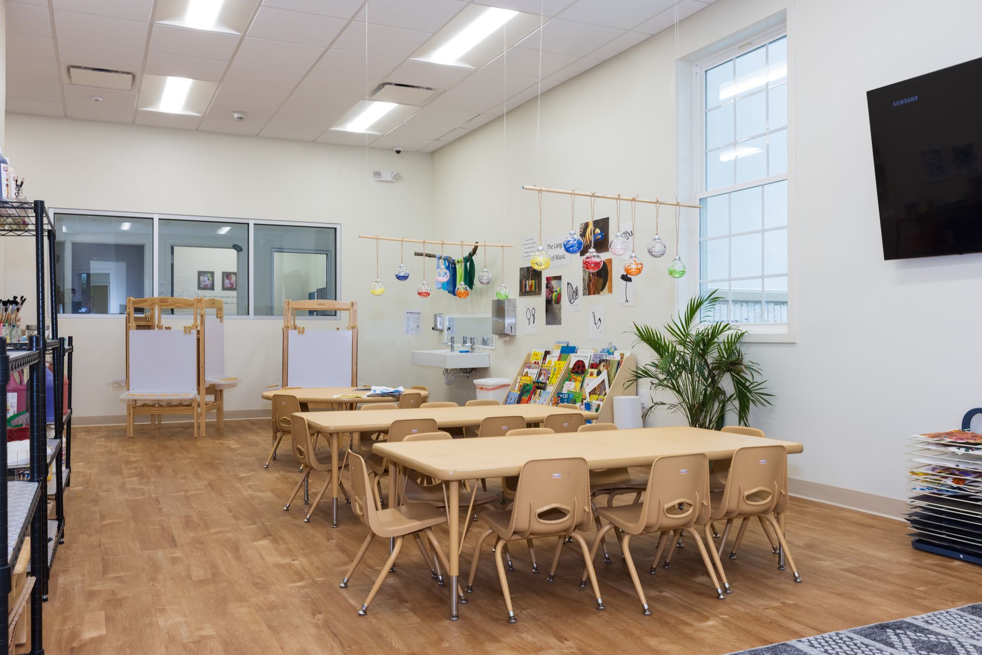 A classroom with tables and chairs and a television on the wall.