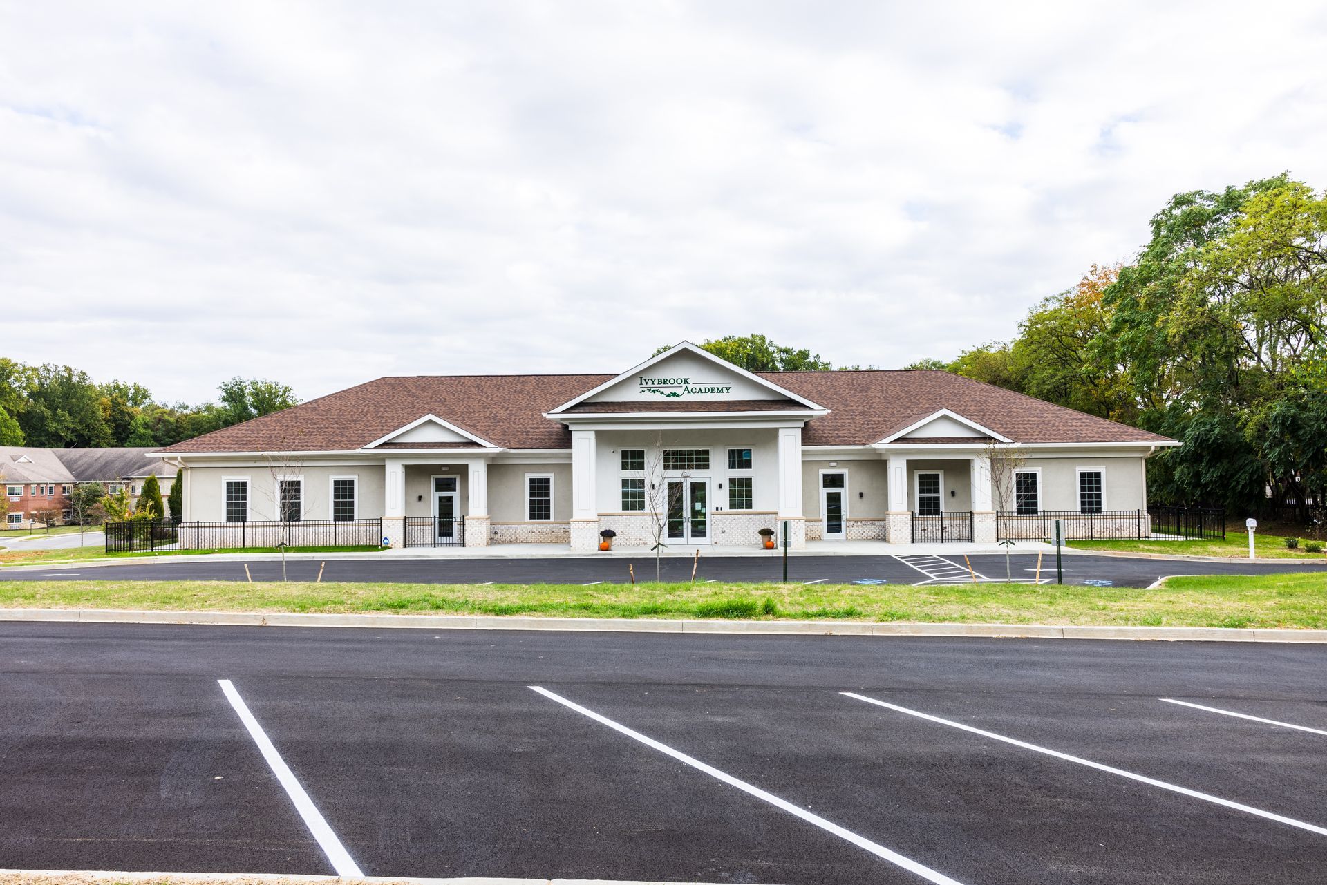 A large white building with a brown roof is sitting next to a parking lot.