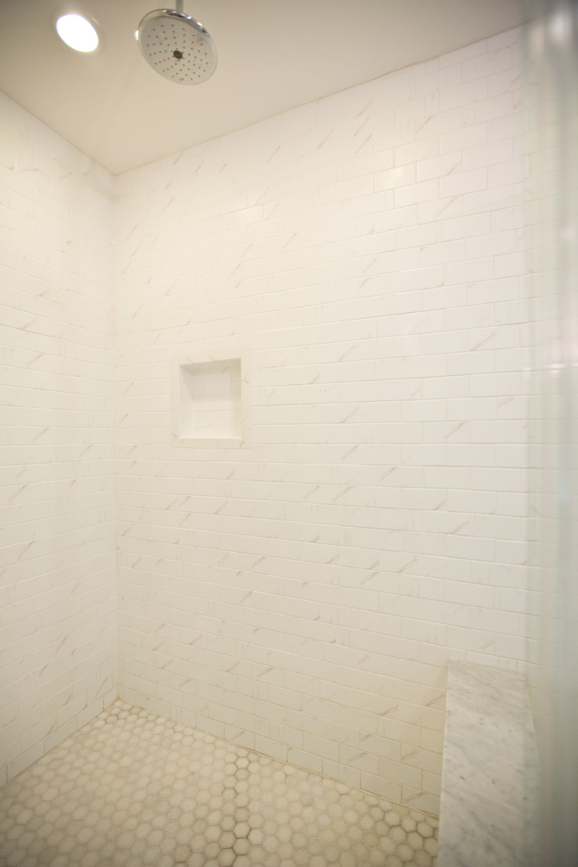 A walk in shower with white tiles and a shower head.