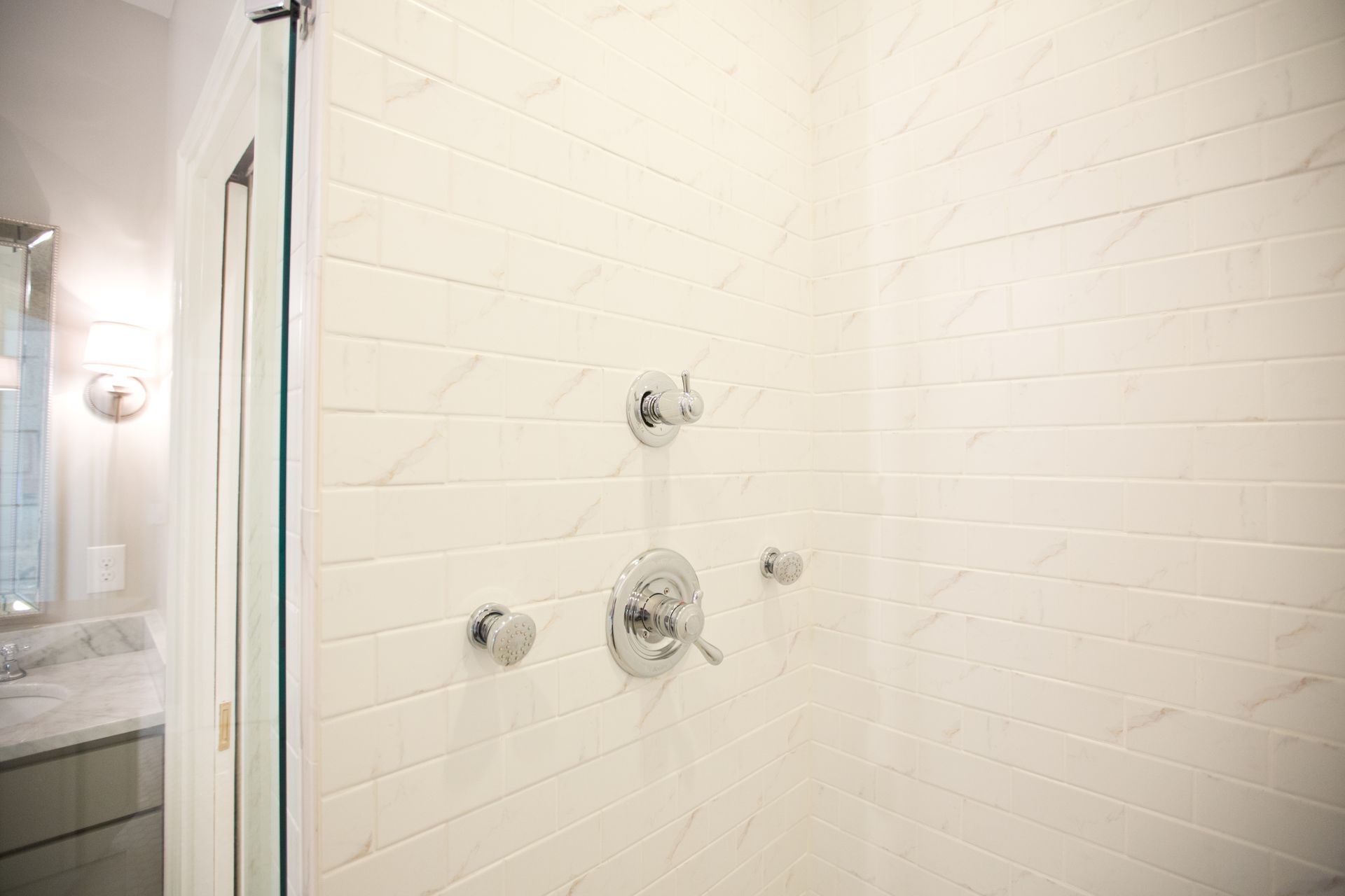 A bathroom with white tiles and a walk in shower with a glass door.