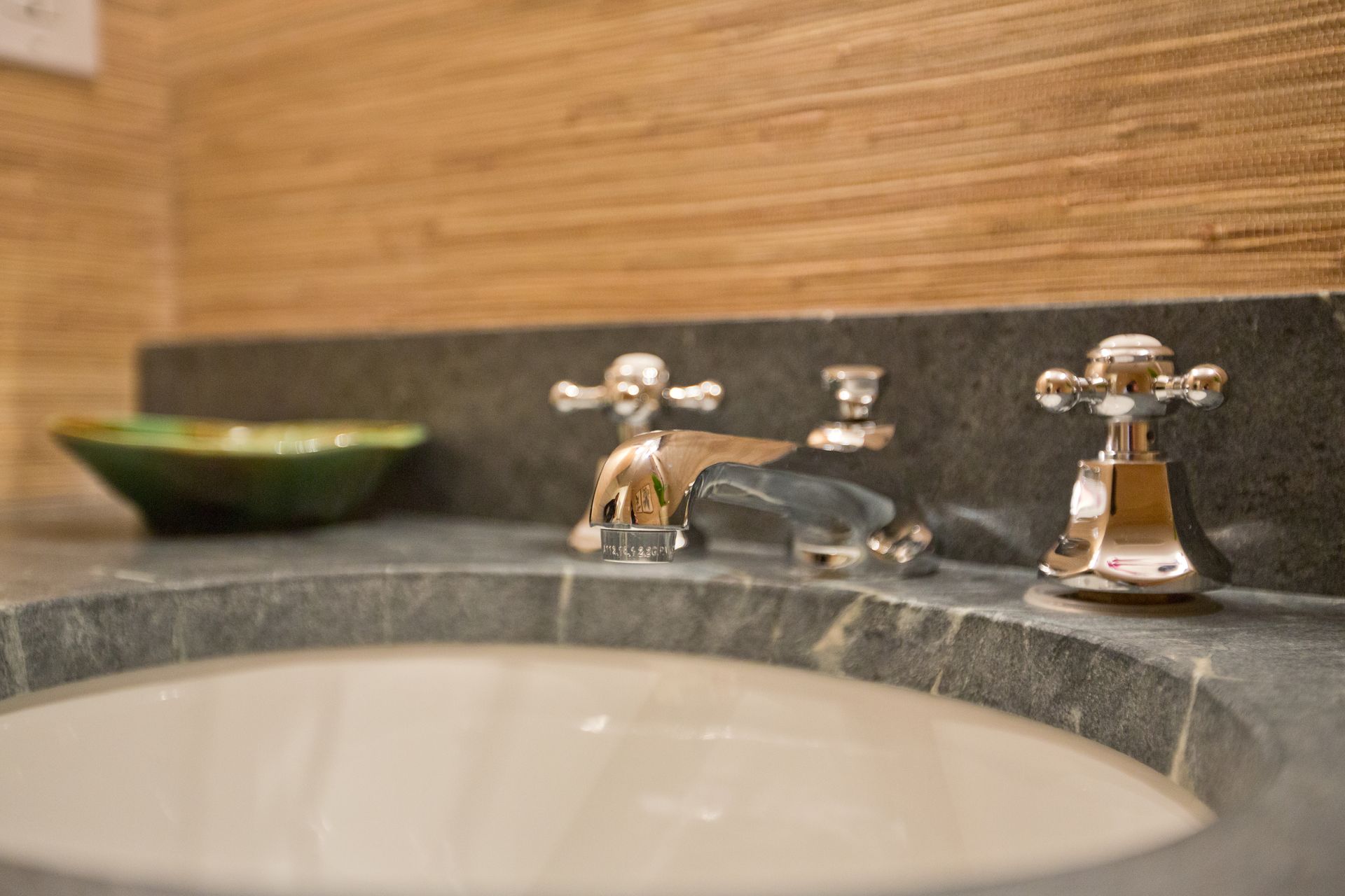 A bathroom sink with three faucets and a bowl on the counter.