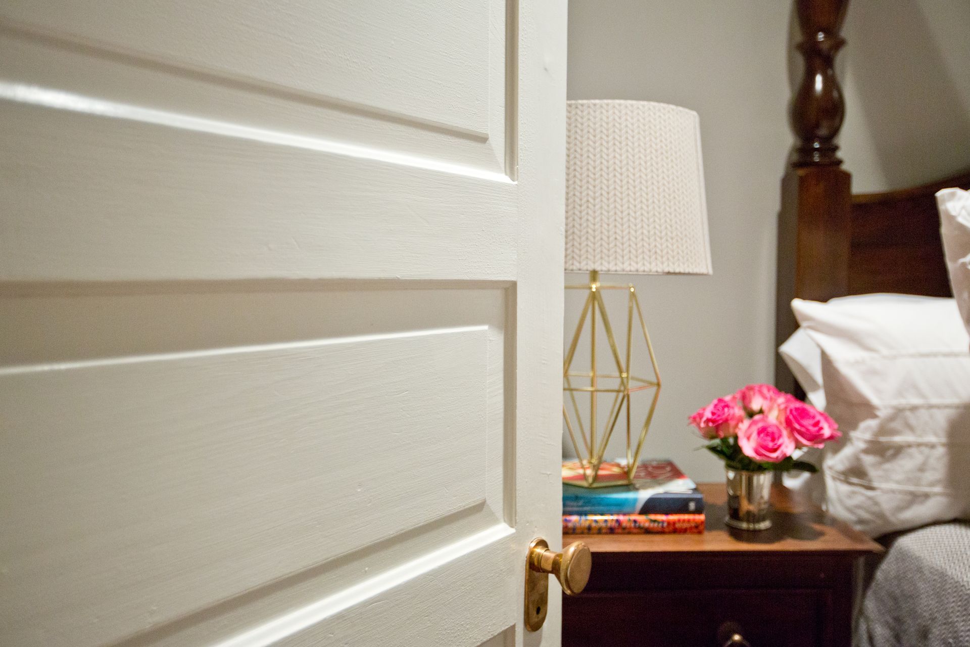 A bedroom with a bed , nightstand , lamp and flowers on the nightstand.