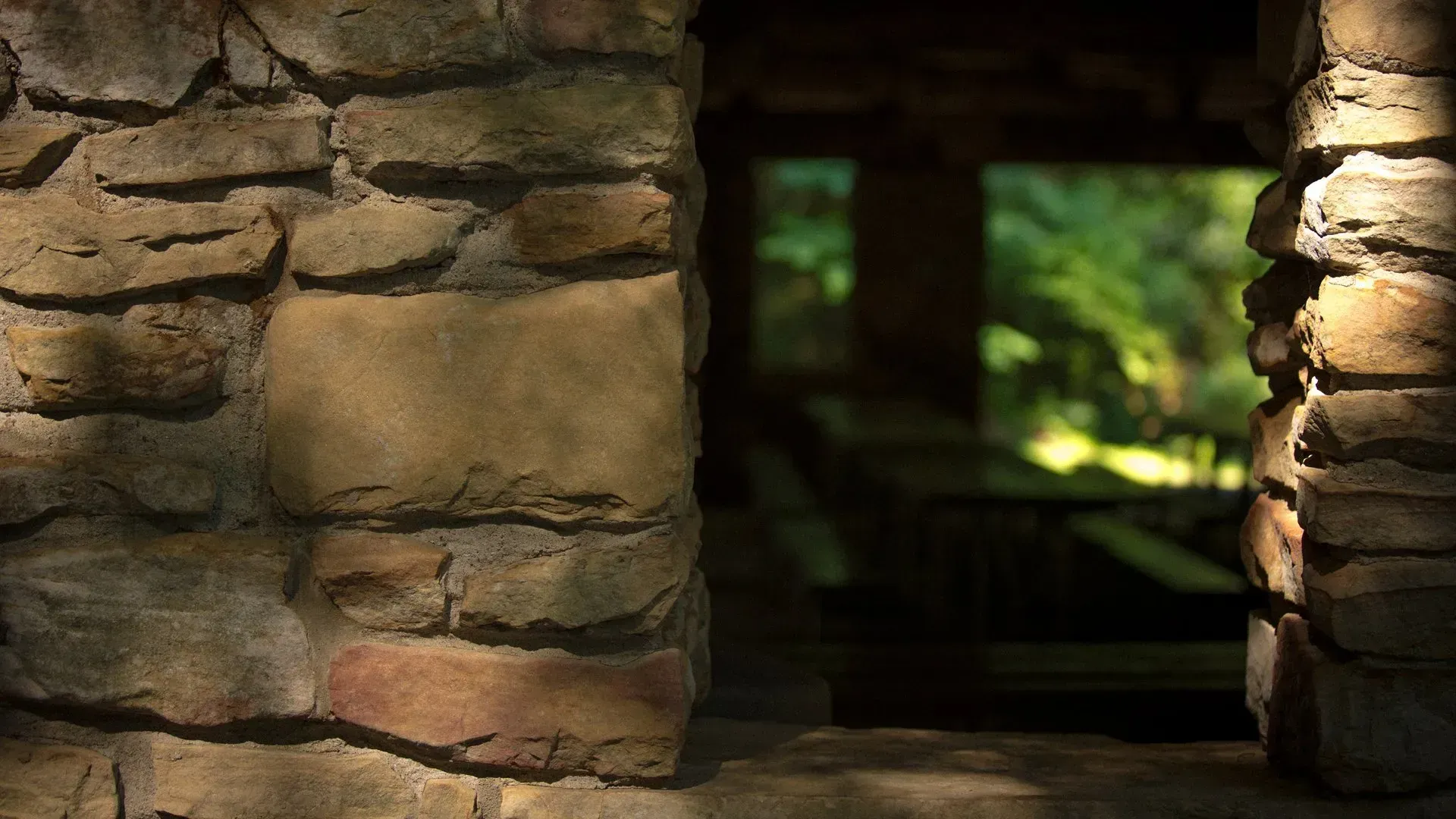 A stone wall with a window looking out to a forest.