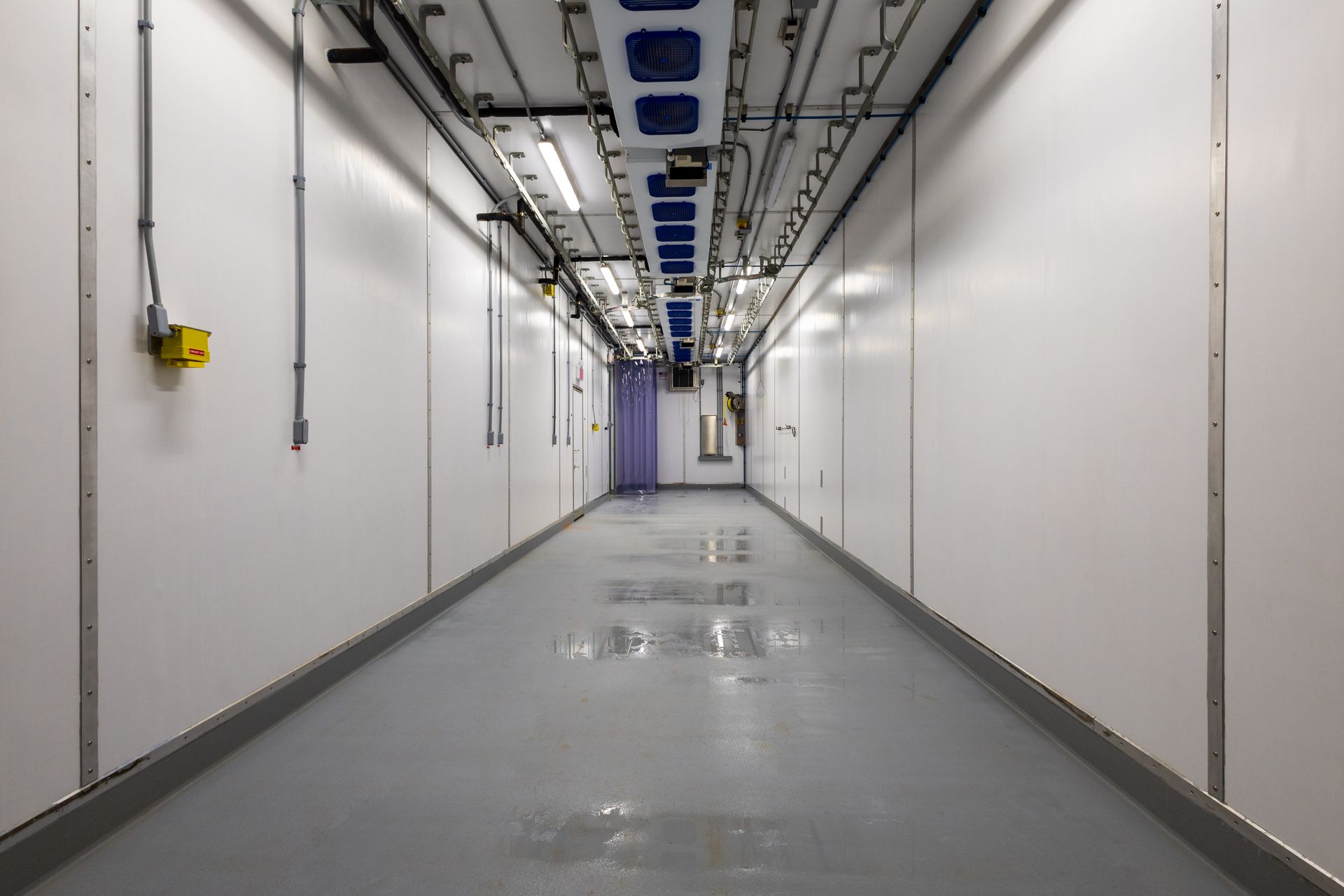 A long hallway with white walls and a gray floor in a building.
