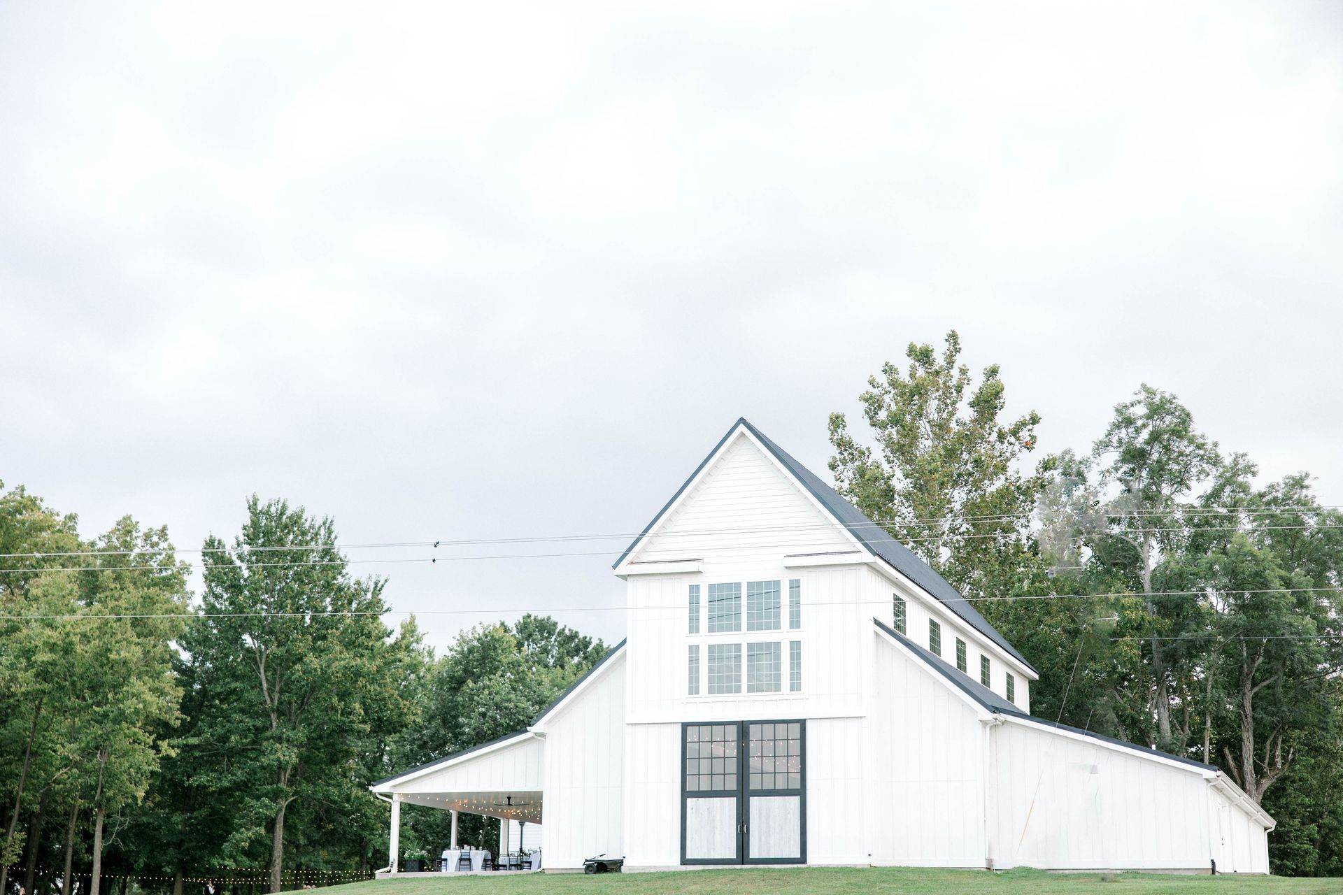 A white barn is sitting on top of a lush green field surrounded by trees.