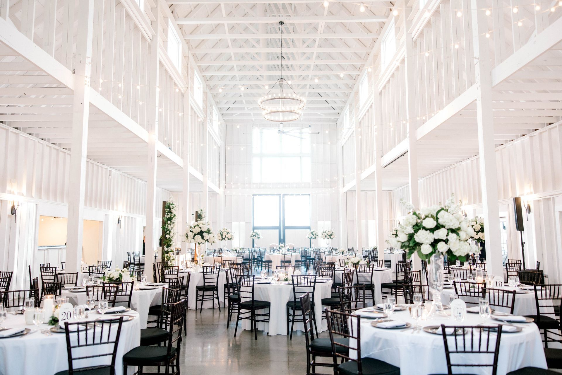 A large white barn filled with tables and chairs for a wedding reception.