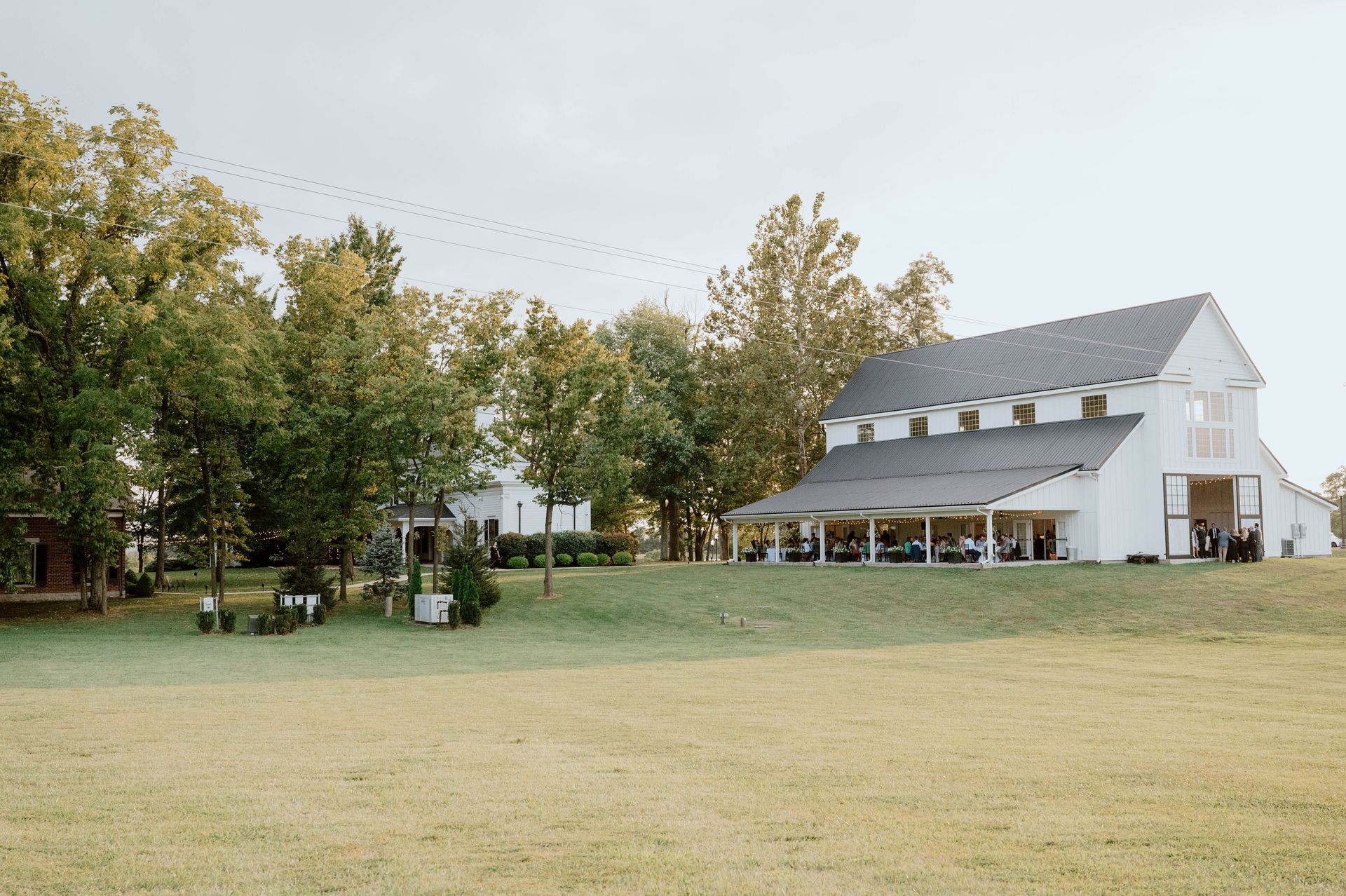 A large white barn is sitting in the middle of a grassy field surrounded by trees.