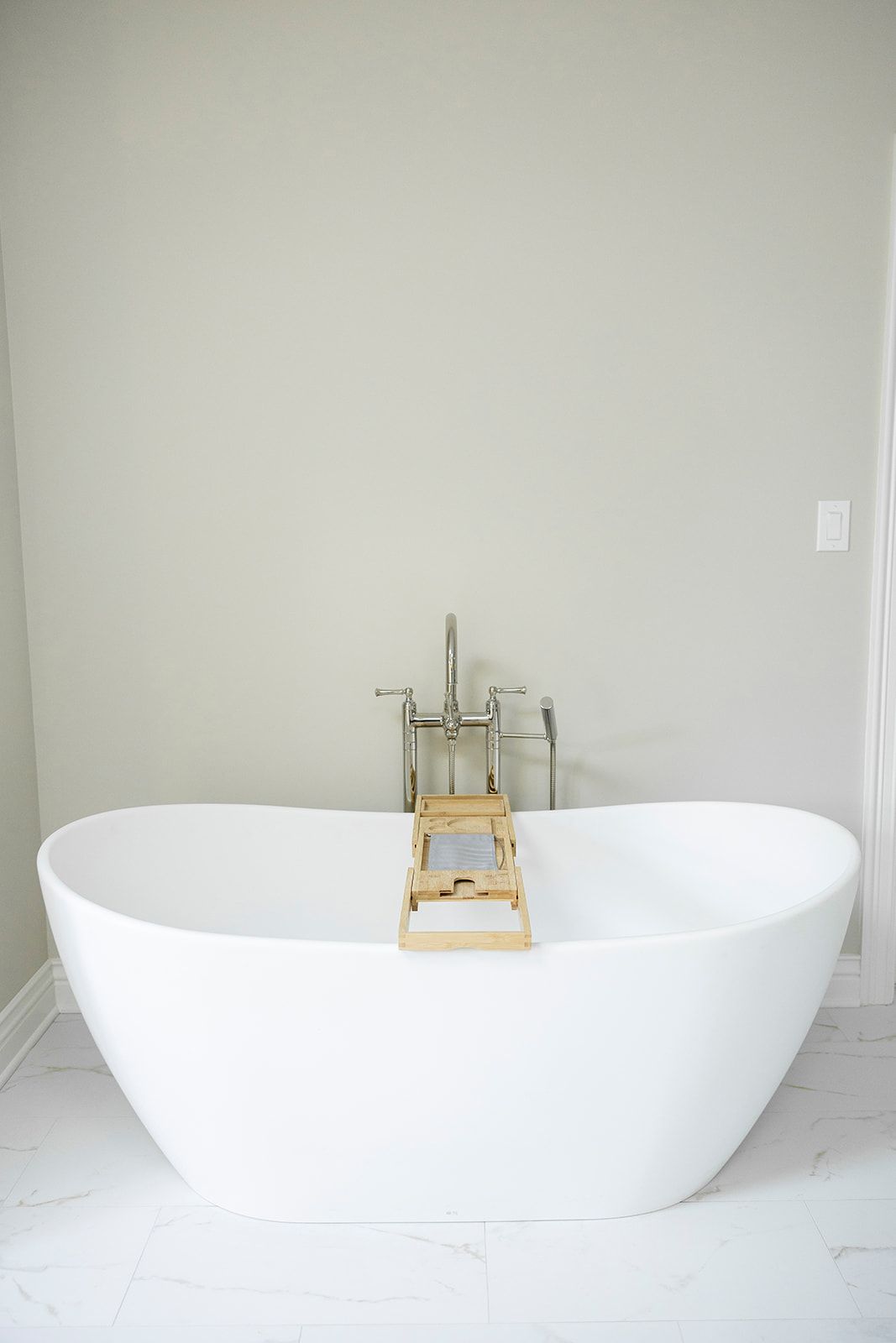 A white bathtub with a wooden tray on top of it in a bathroom.