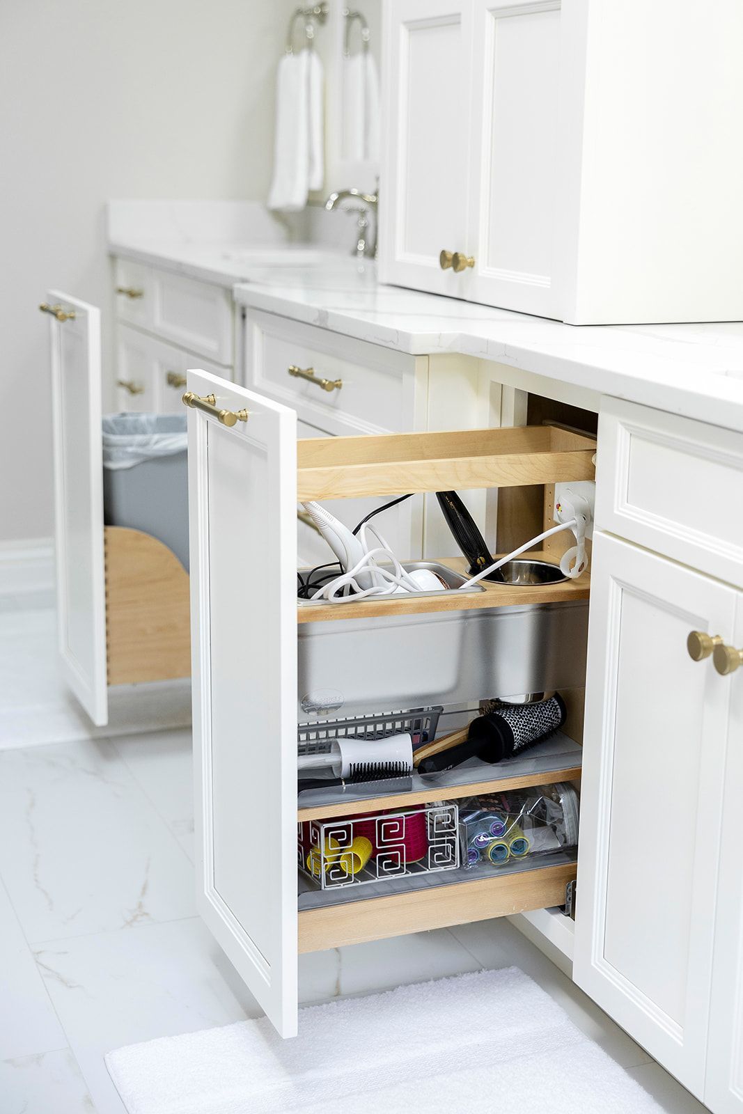 A bathroom with white cabinets and a pull out drawer filled with cleaning supplies.
