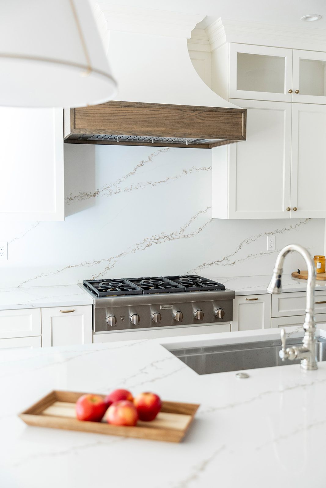 A kitchen with white cabinets , a stove top oven , a sink , and a wooden hood.
