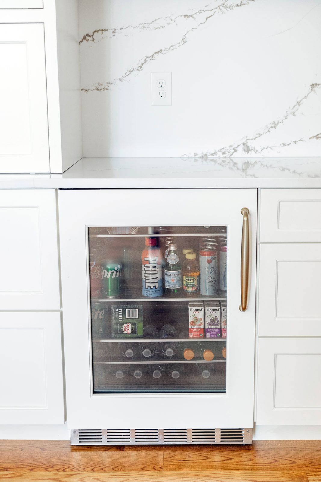 A refrigerator filled with bottles and cans of soda in a kitchen.