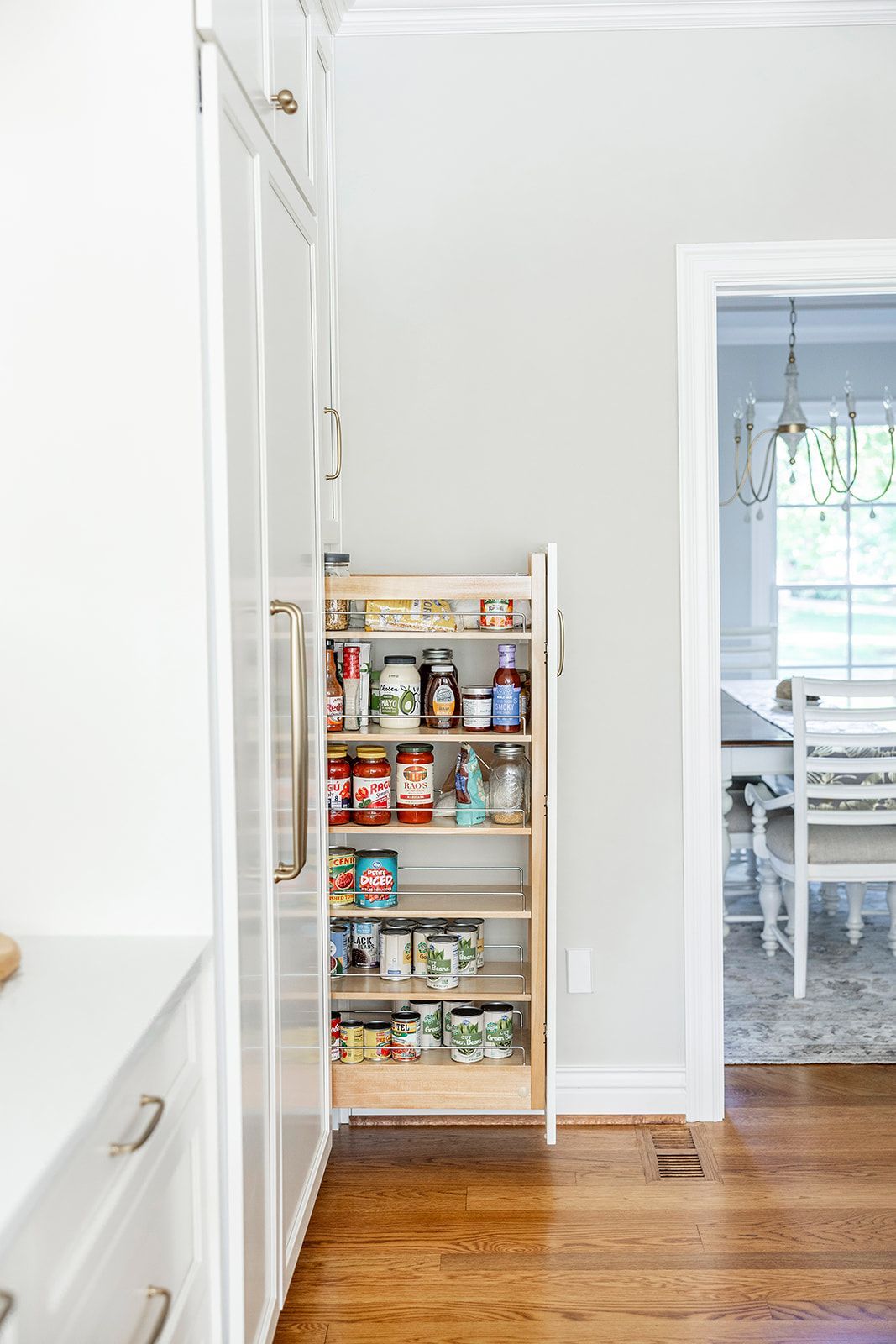 A kitchen with a pull out pantry and a dining room in the background.