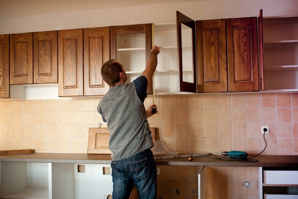 A man is measuring a cabinet in a kitchen.